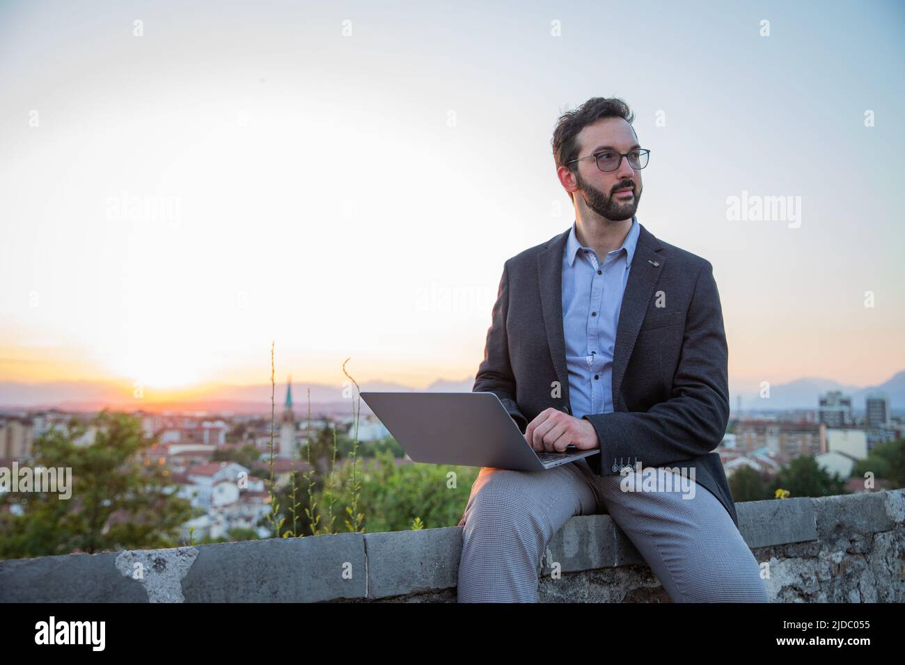 Elegantly dressed businessman uses his laptop outside with sunset Stock Photo