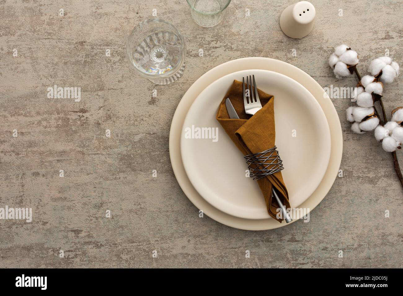 Table setting, plate with napkin and cutlery on a brown background, top view of the served table decorated with dry flowers Stock Photo