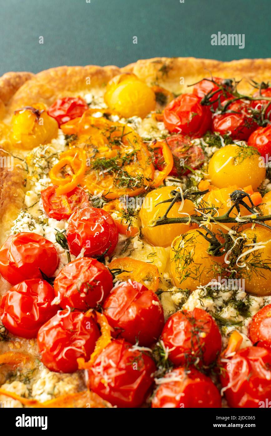 Homemade pie made of puff pastry and yellow, orange and red tomatoes, savory square pie on a green background, top view, copy space Stock Photo