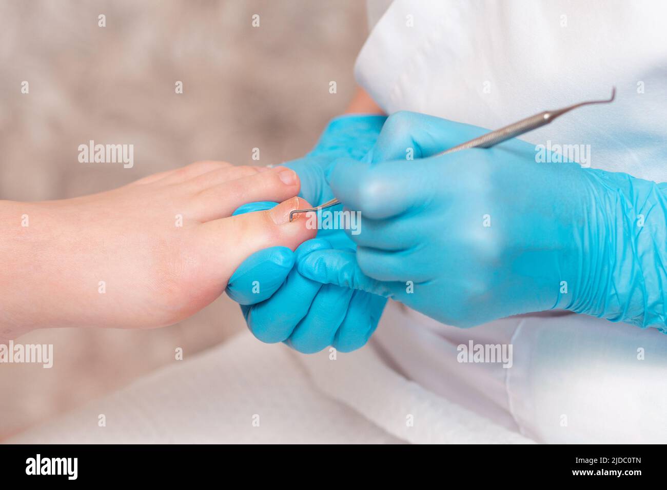 Pedicurist does a pedicure for the client's foot, cleaning the nails with a doublesided curette