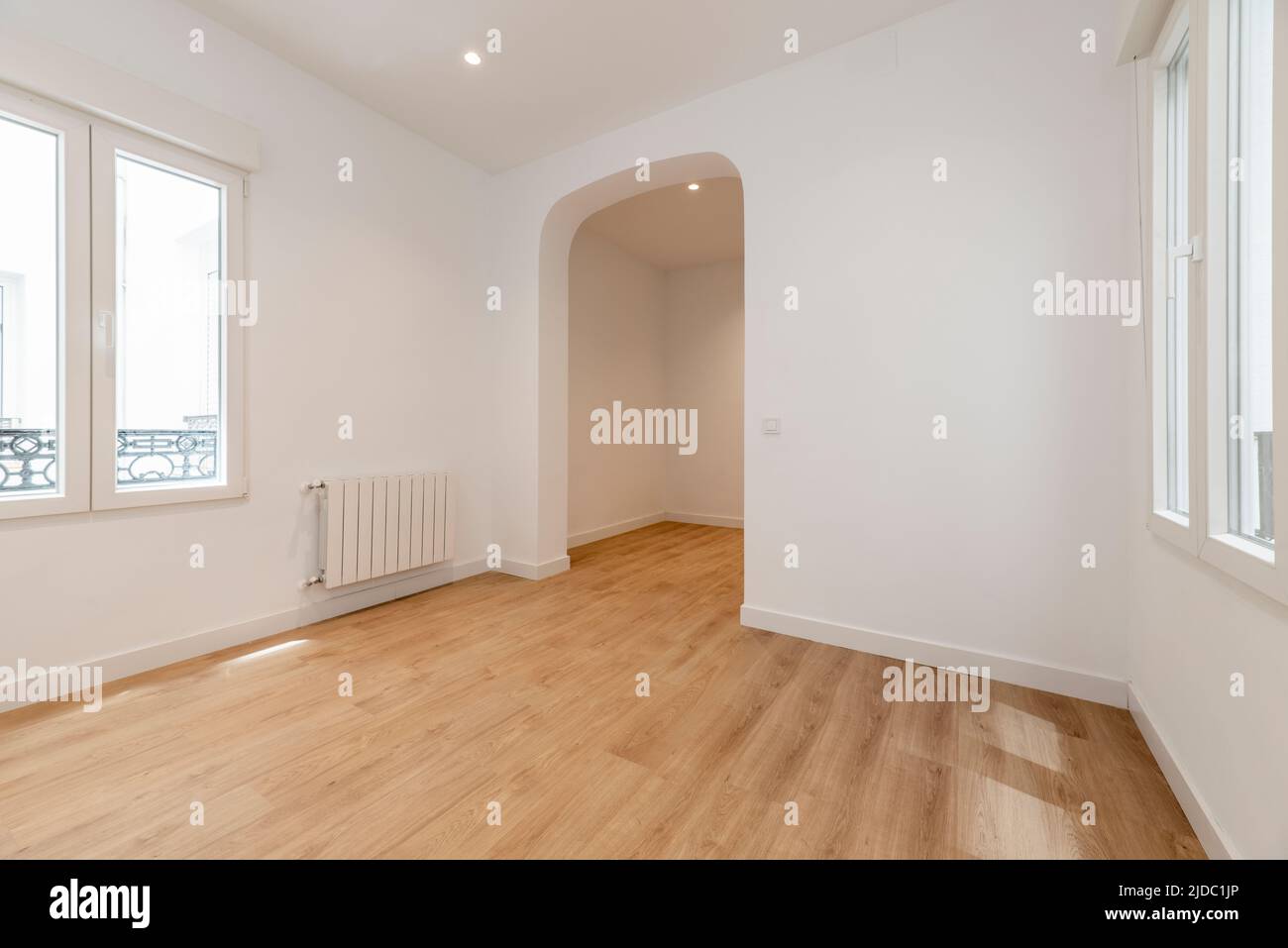 Empty room with white painted walls, oak laminate flooring, white aluminum windows and basket weave between rooms Stock Photo