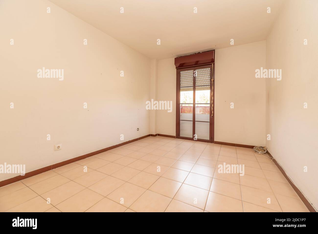 Empty room with plain white painted walls, ceramic tiled floor and reddish aluminum joinery on balcony doors Stock Photo