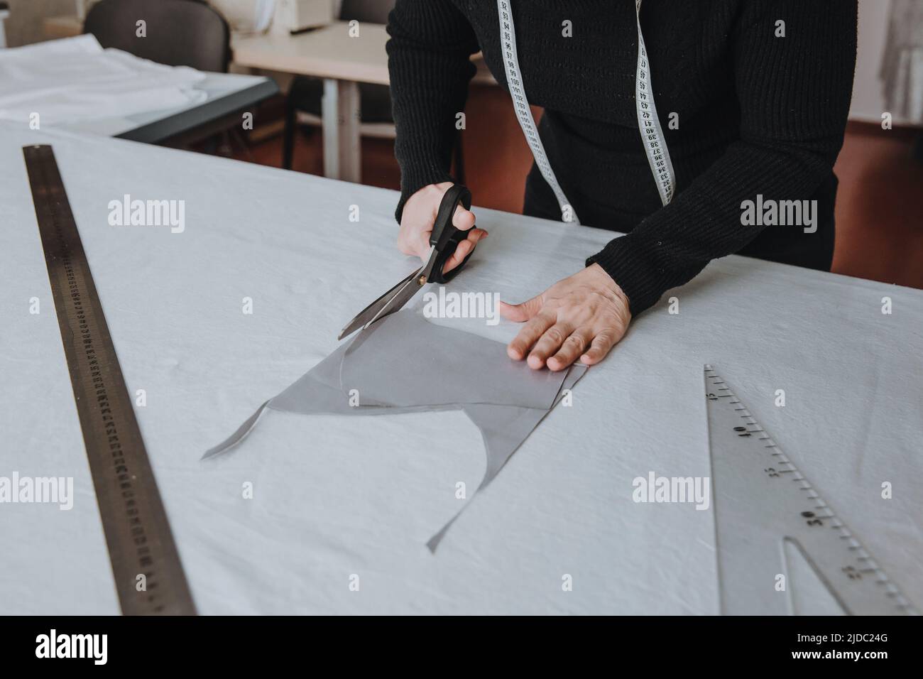 Tailor designer working of cutting piece of cloth with scissors, a triangle and a ruler lie on the table nearby, entrepreneur concept. Stock Photo
