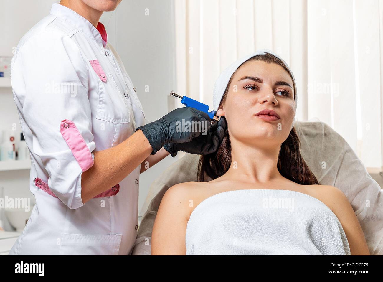 Portrait of woman having ear piercing process. Specialist pierces the