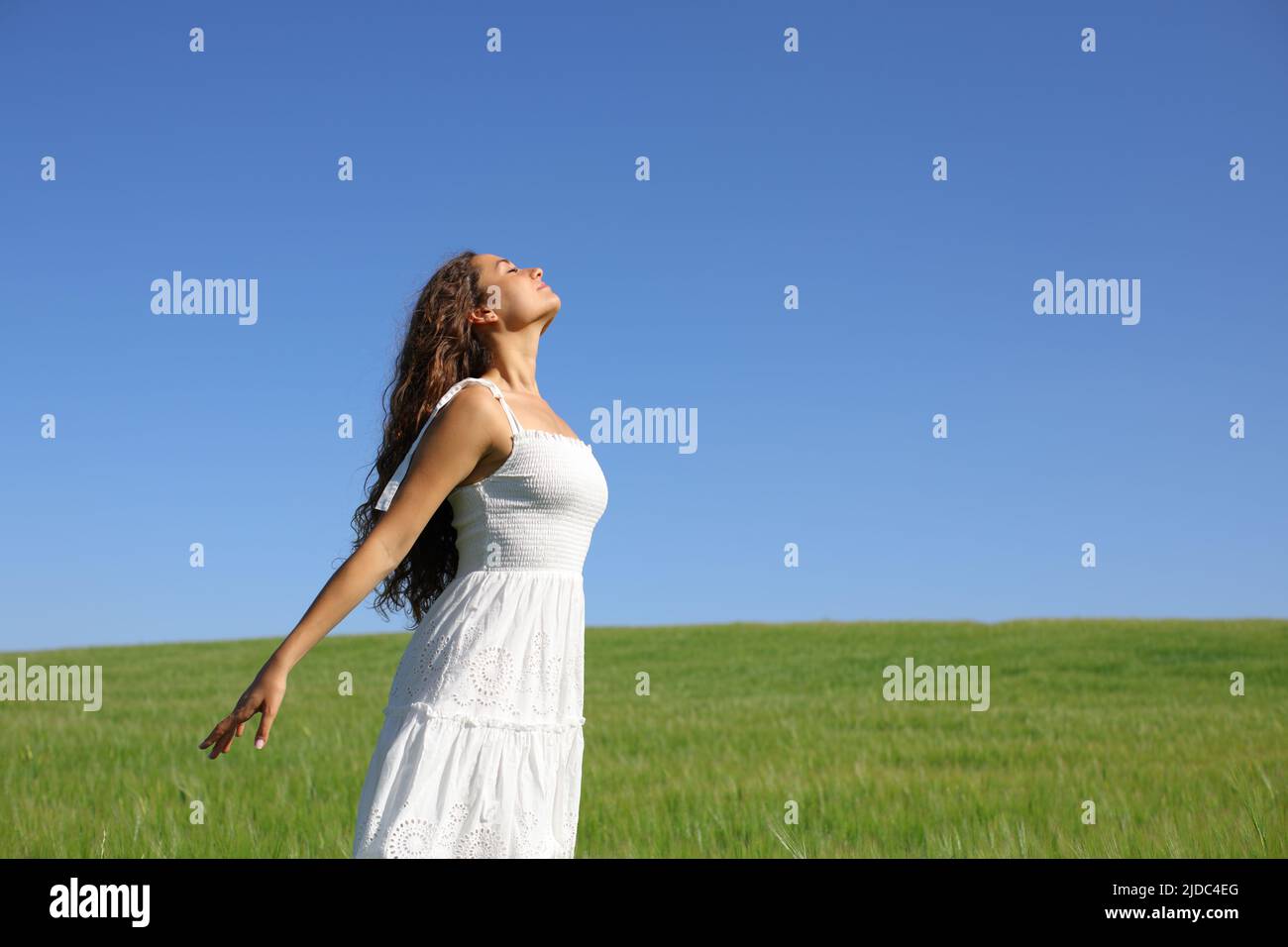 Profile of a woman in white dress breathing fresh air in a green wheat ...