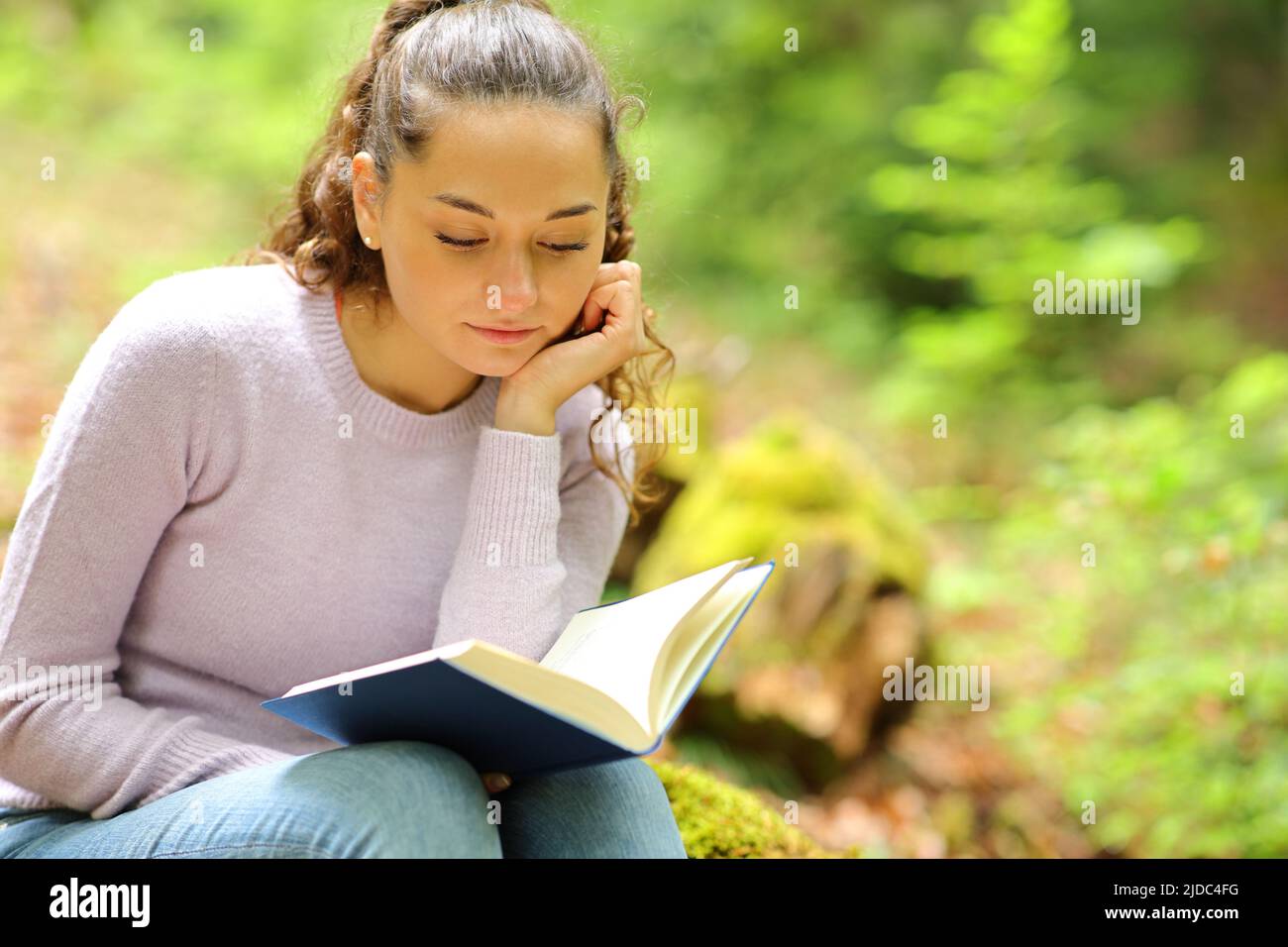 Relaxed woman reading a book in a green forest Stock Photo