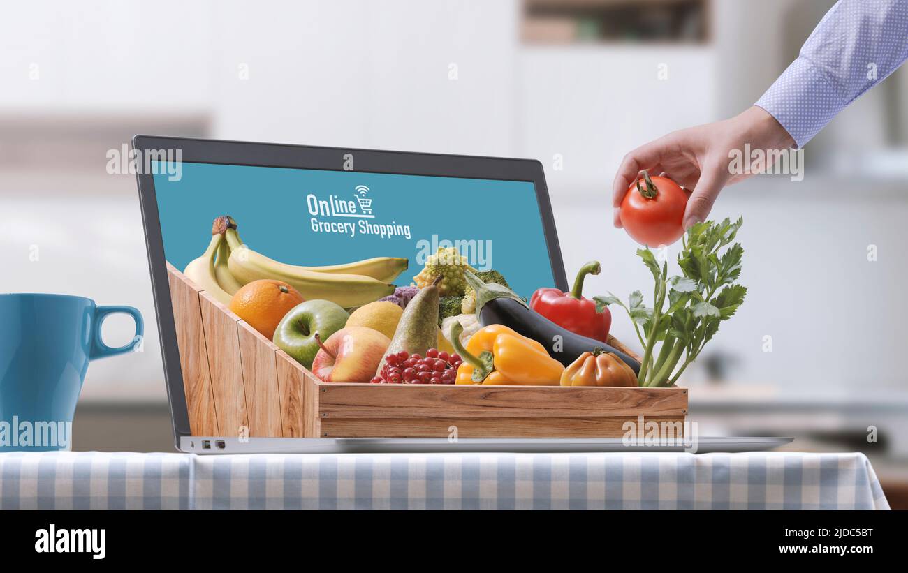 Crate full of fresh vegetables and fruit on a laptop at home, online grocery shopping concept Stock Photo