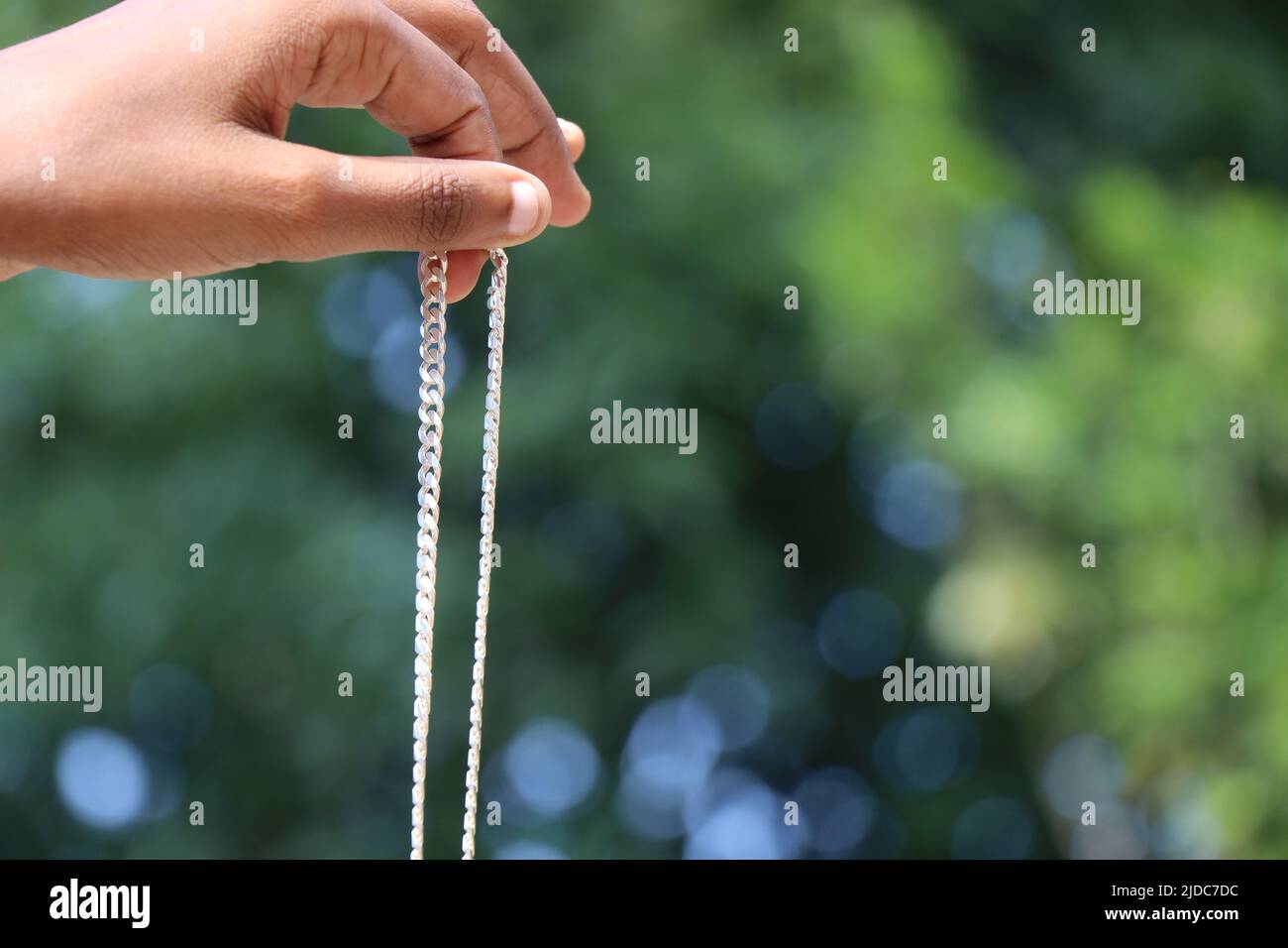 Holding a new silver chain in hand on green nature background Stock Photo