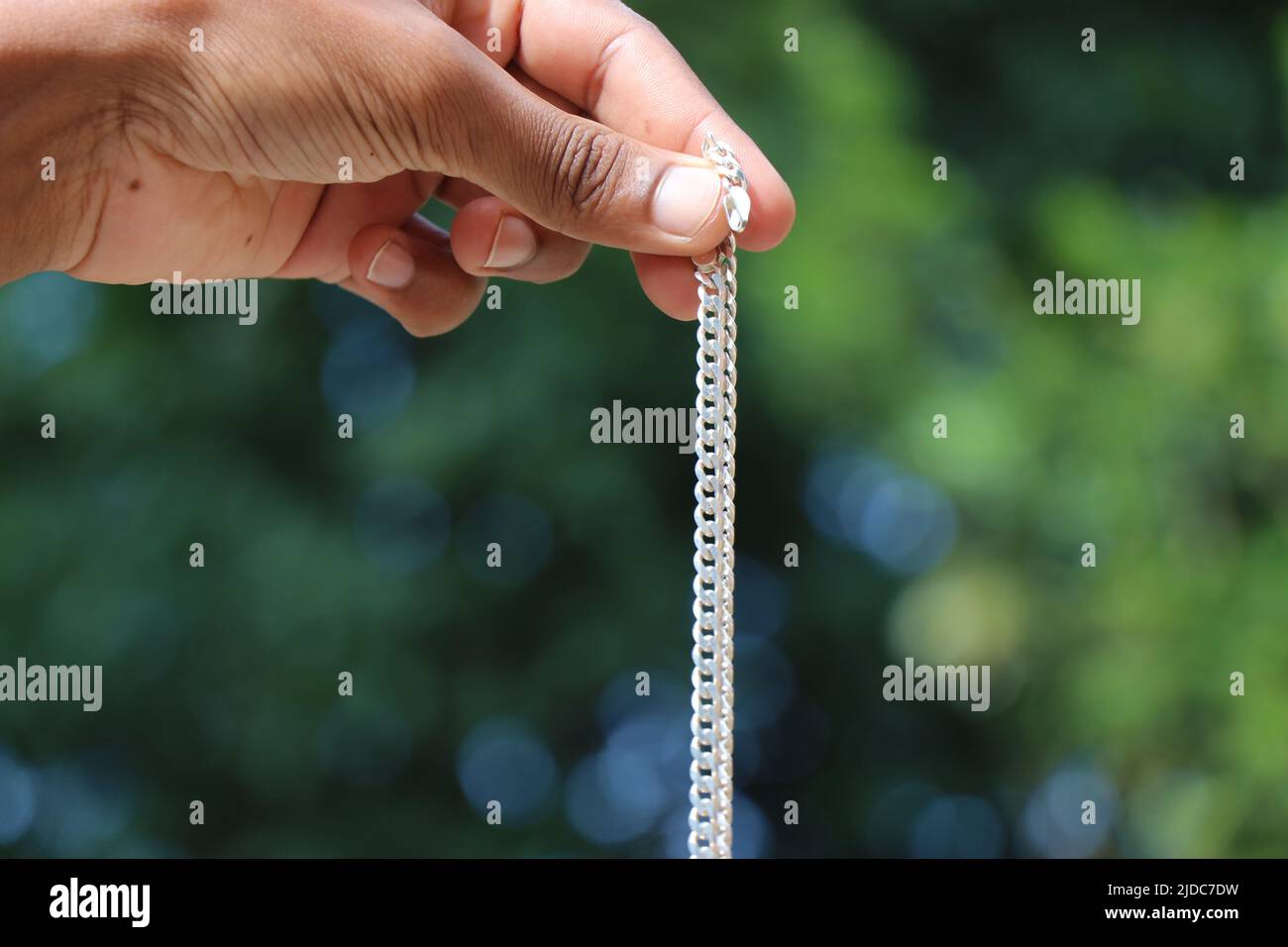 The silver chain held in hand on natural green background Stock Photo