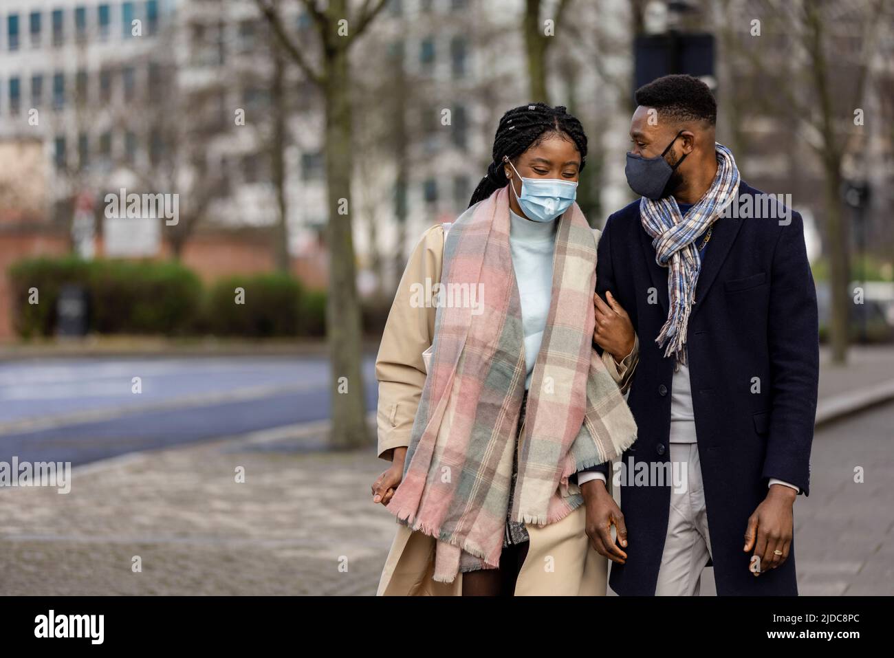Couple with face coveings walking arm in arm in city cente Stock Photo