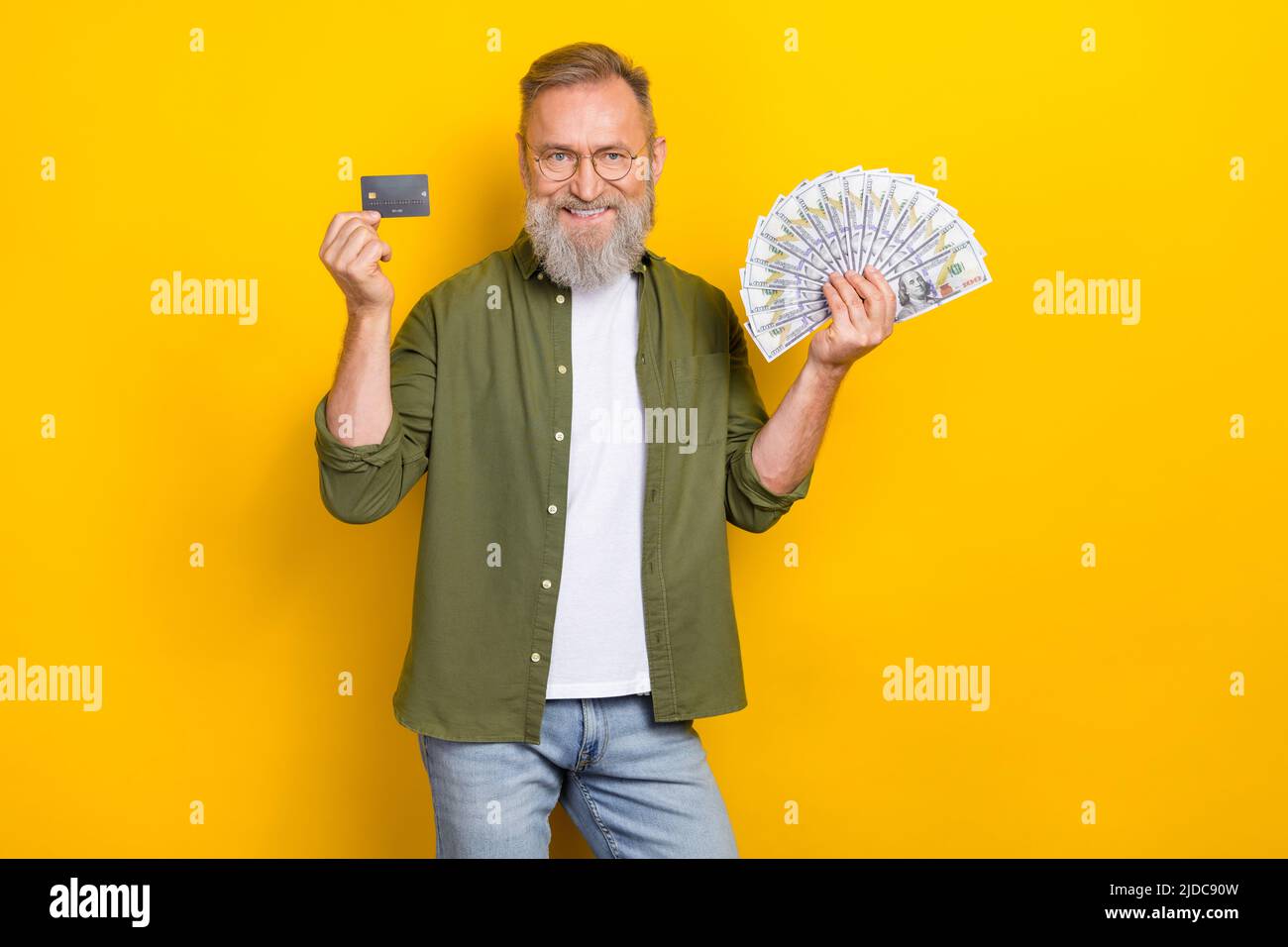 Portrait of cheerful successful person hold dollars cash debit plastic card isolated on yellow color background Stock Photo