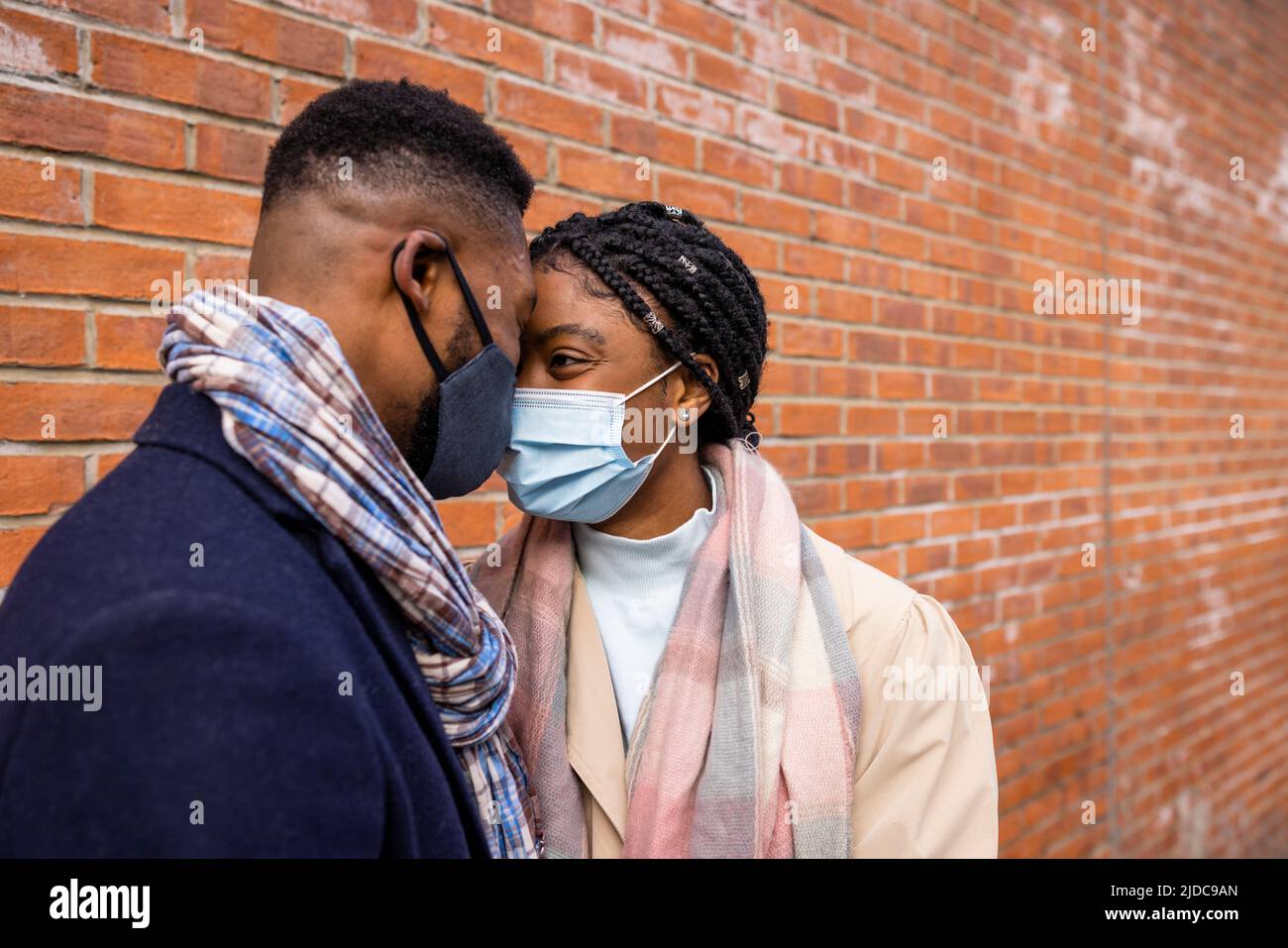 Couple wearing face masks facing each other by brick wall Stock Photo