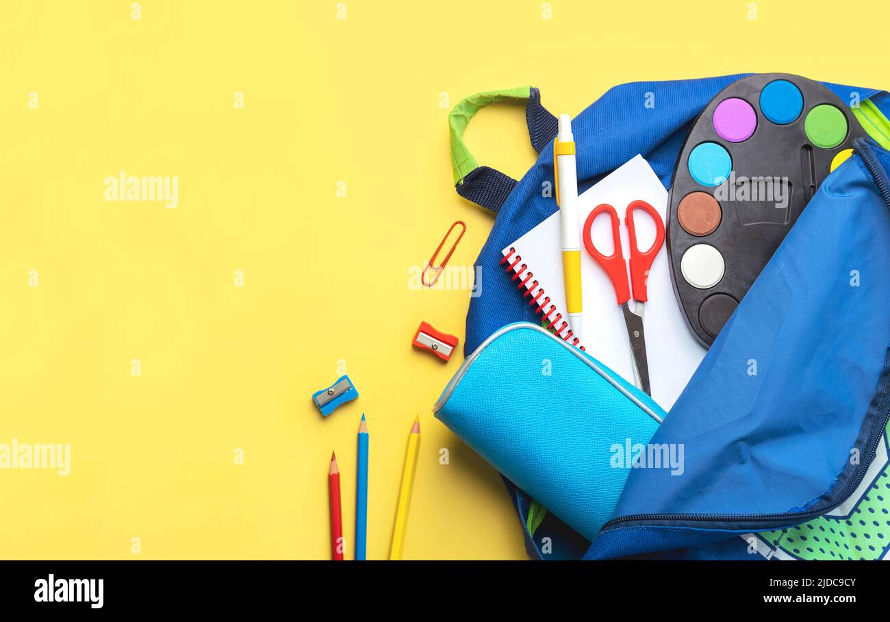 Top view of school backpack and school supplies with space for text on yellow background. Back to school concept Stock Photo