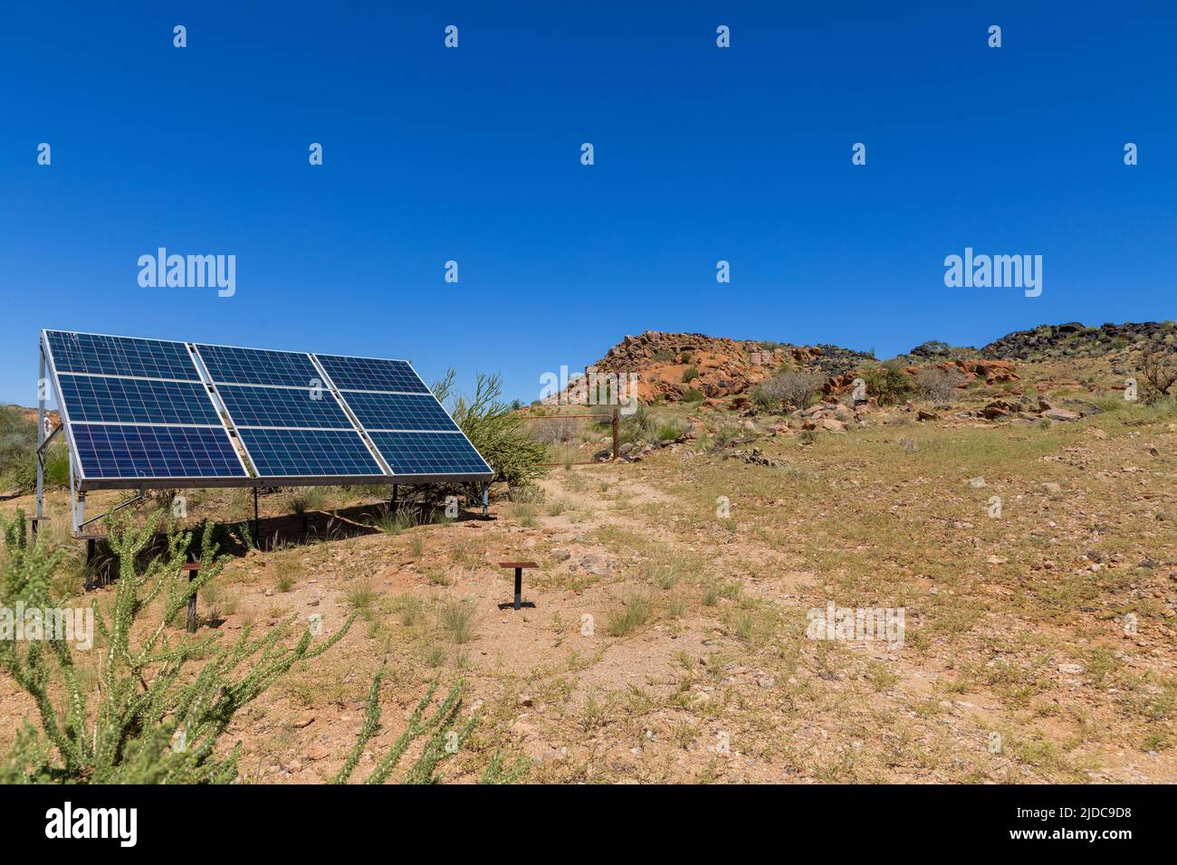 Isolated dry semi desert area with rocks and grassy sandy areas.  Nine solar panels mounted on a metal frame to provide electricity. Stock Photo