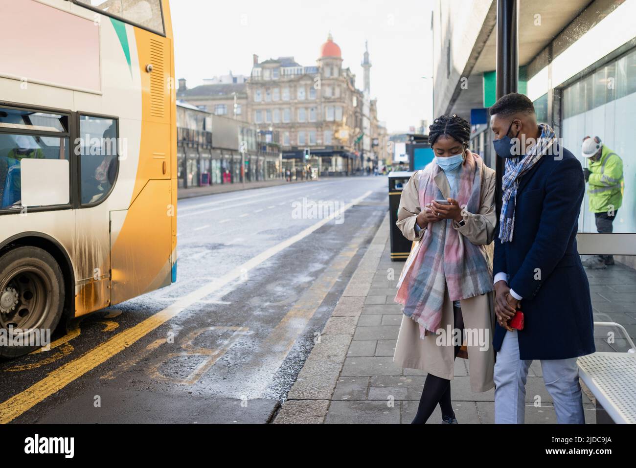 Couple waiting for bus weraing face coverings, looking at app on mobile, checking bus times Stock Photo