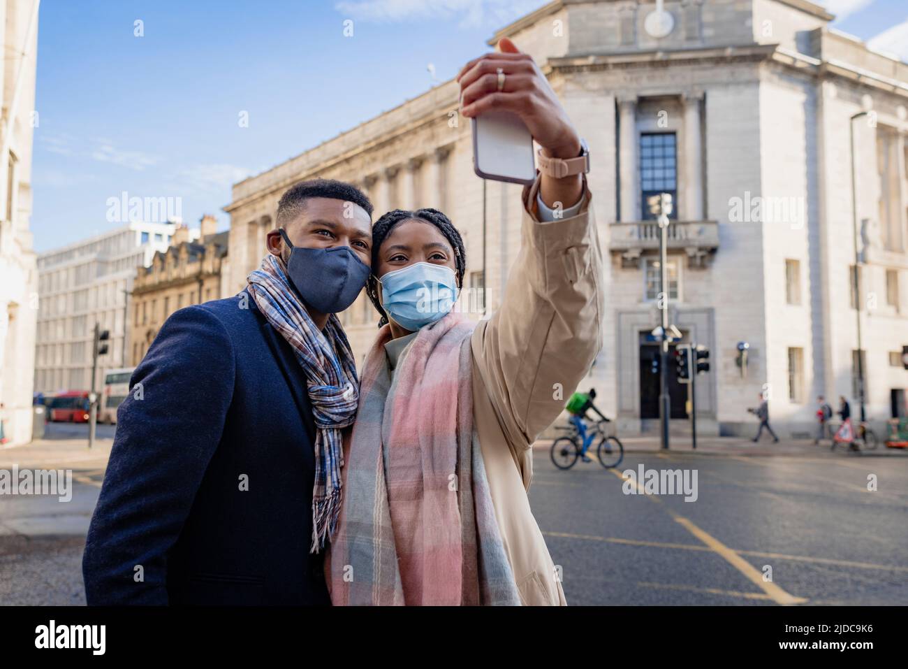 Couple in town wearing face masks holding mobile phone and taking selfie Stock Photo