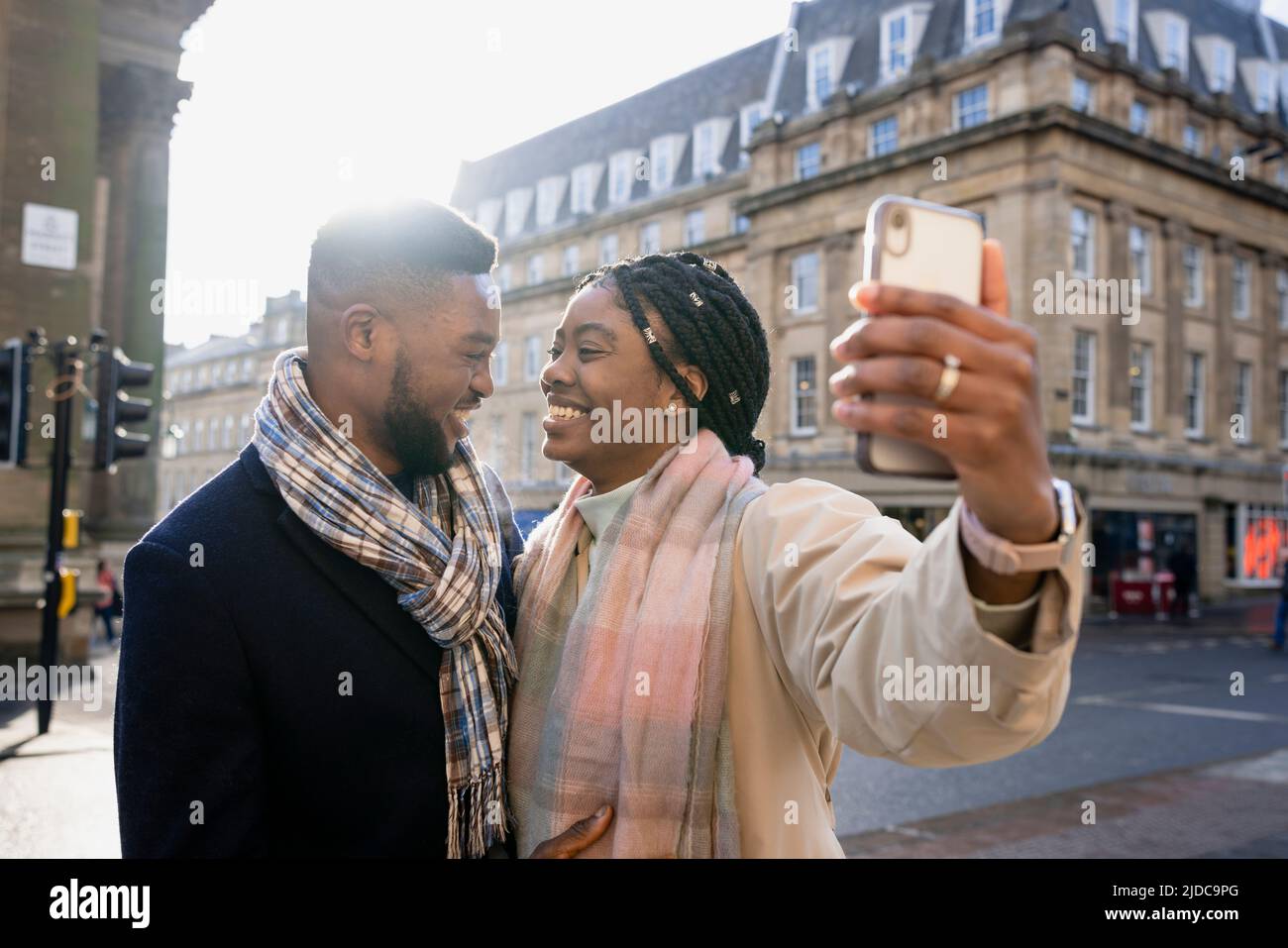 Cheerful couple smiling face to face in town, woman holding phone taking selfie Stock Photo