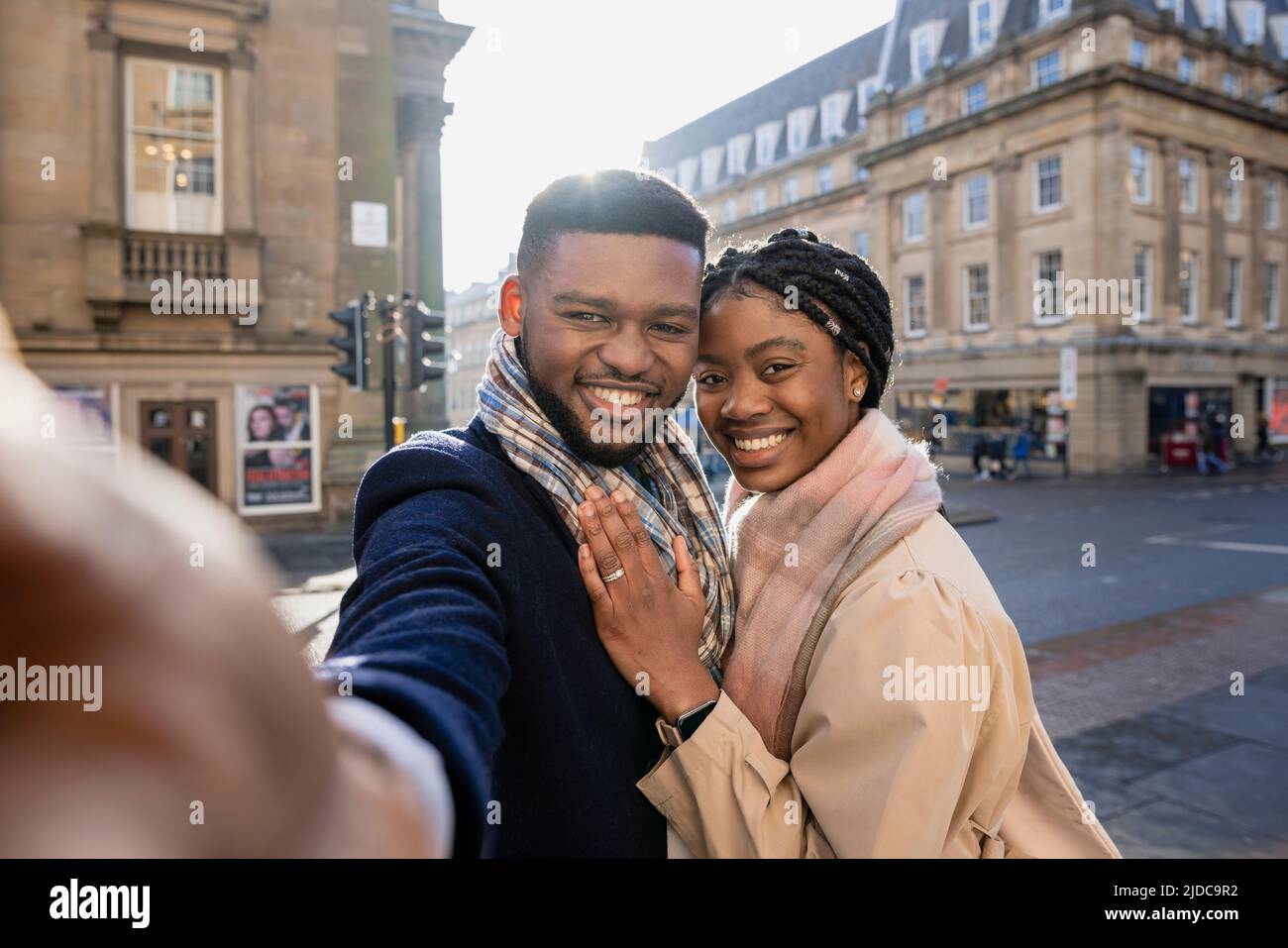 Cheerful couple in town taking selfie with mobile phone, woman with hand on man's chest Stock Photo