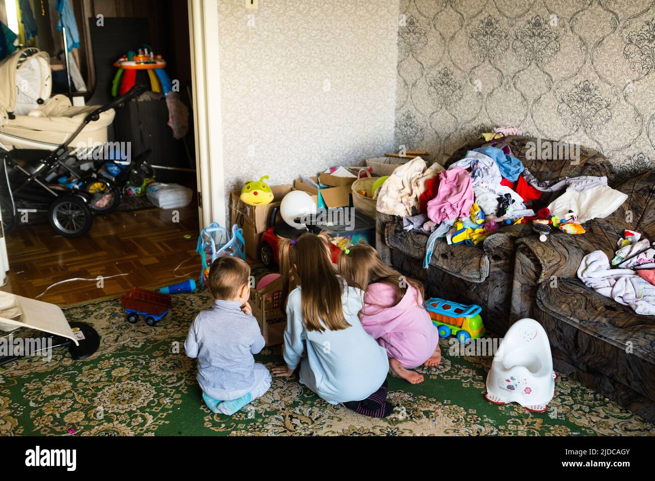 Three unrecognizable children are playing in a dirty cluttered room. Stock Photo