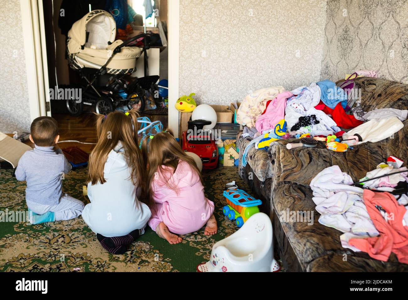 Three unrecognizable children are playing in a dirty cluttered room. Stock Photo