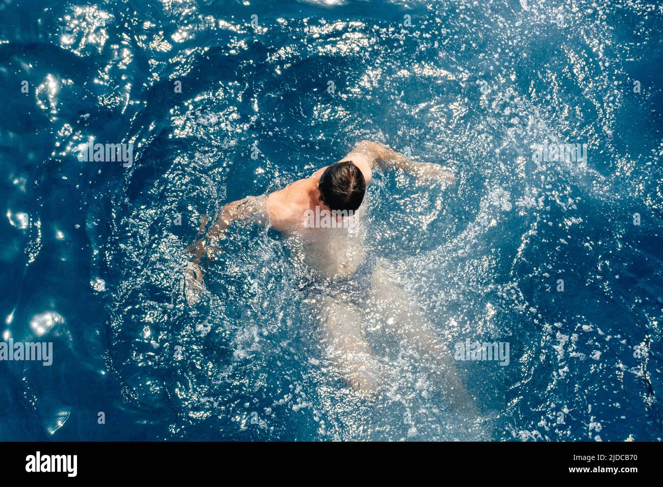 Soft Selective focus Man in blue sea water or pool. The guy dived from the water. Gentle sun glare on the surface. The concept of vacation, travel and enjoyment of a quiet life. Stock Photo