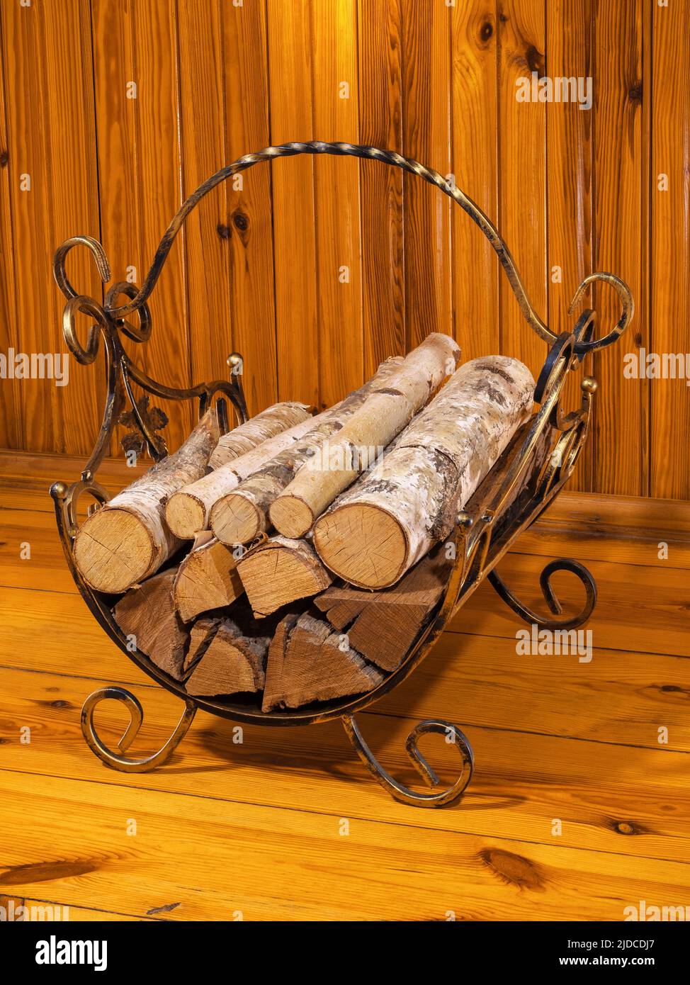 Firewood stack in brass basket by a wooden wall Stock Photo