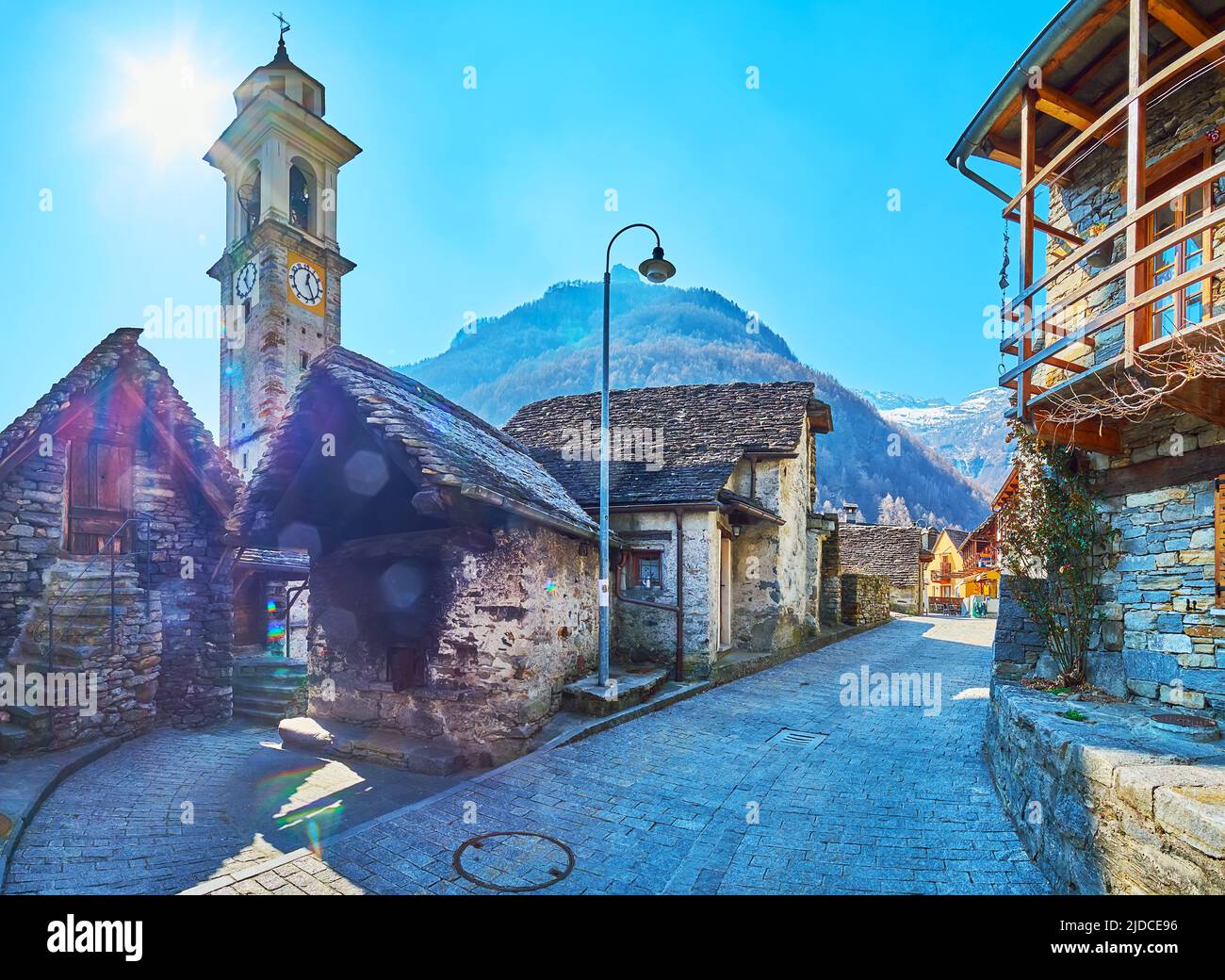 Panorama of sunny street with church's clocktower, stone houses and mountains, Sonogno village, Valle Verzasca, Switzerland Stock Photo