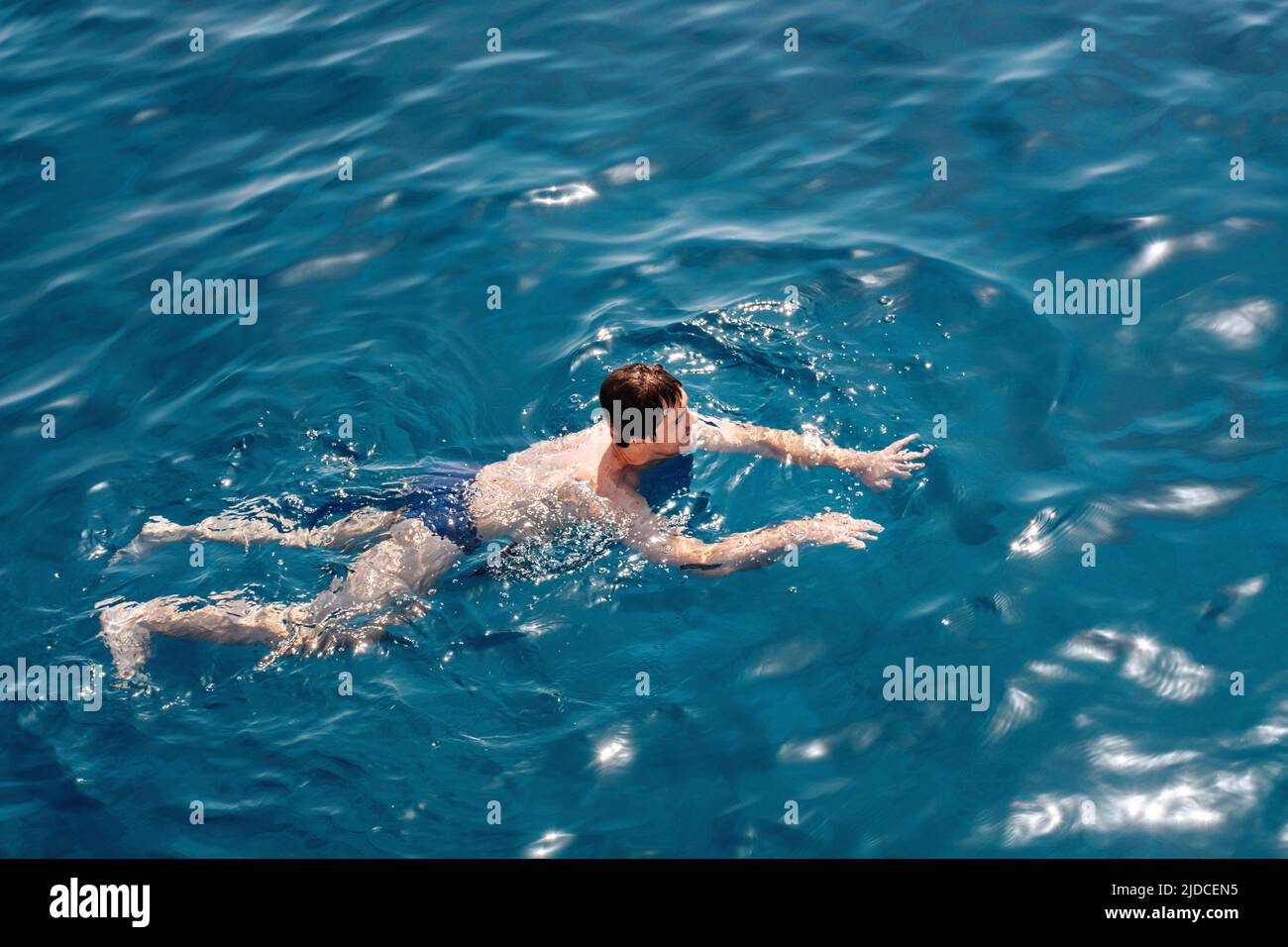 The guy swims in the blue calm sea water or ocean. Gentle sun glare on the surface. The concept of vacation, travel and enjoyment of a quiet life. Soft selective focus. Stock Photo