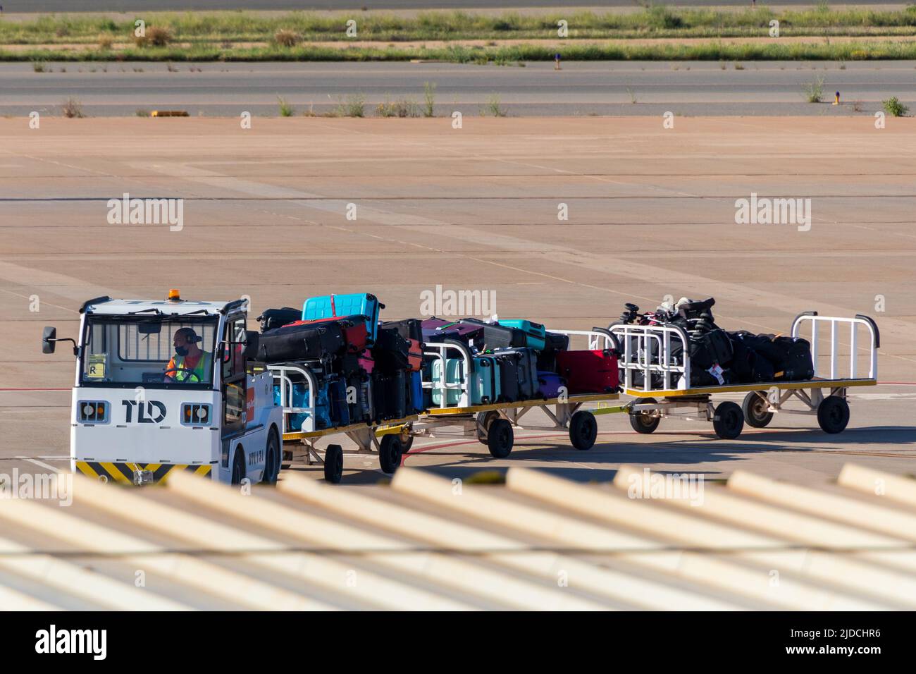 Baggage Handlers, Suitcases and Bags Being Transported From The Aircraft For Collection At Arrivals Stock Photo