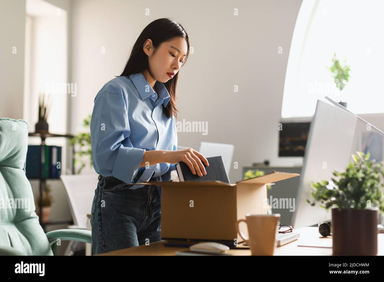 Fired Asian Woman Packing Belongings In Box After Dismissal Indoor Stock Photo