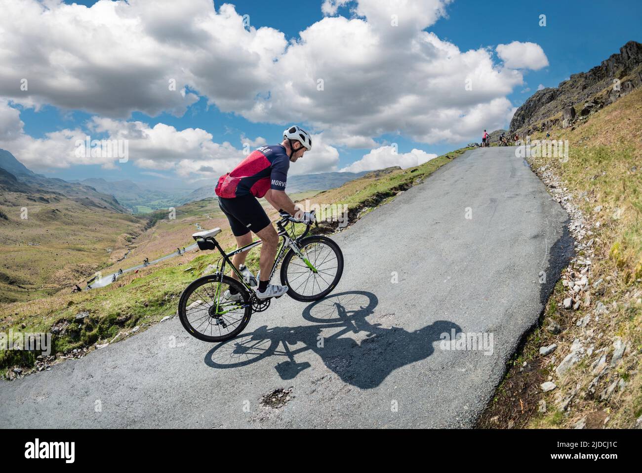 Late afternoon and a cyclist riding up Hardknott Pass in the Fred Whitton Challenge cycling sportive held in the English Lake District, UK. Stock Photo