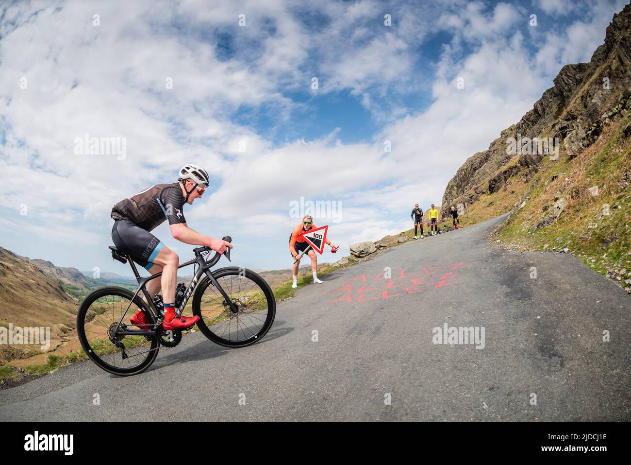 Simon Warren encourging a cyclist riding up Hardknott Pass in the Fred Whitton Challenge cycling sportive held in the English Lake District, UK. Stock Photo