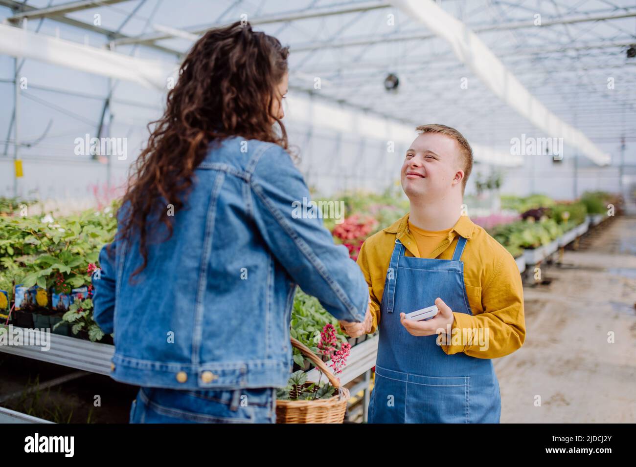 Happy young employee with Down syndrome working in garden centre, taking payment from customer. Stock Photo