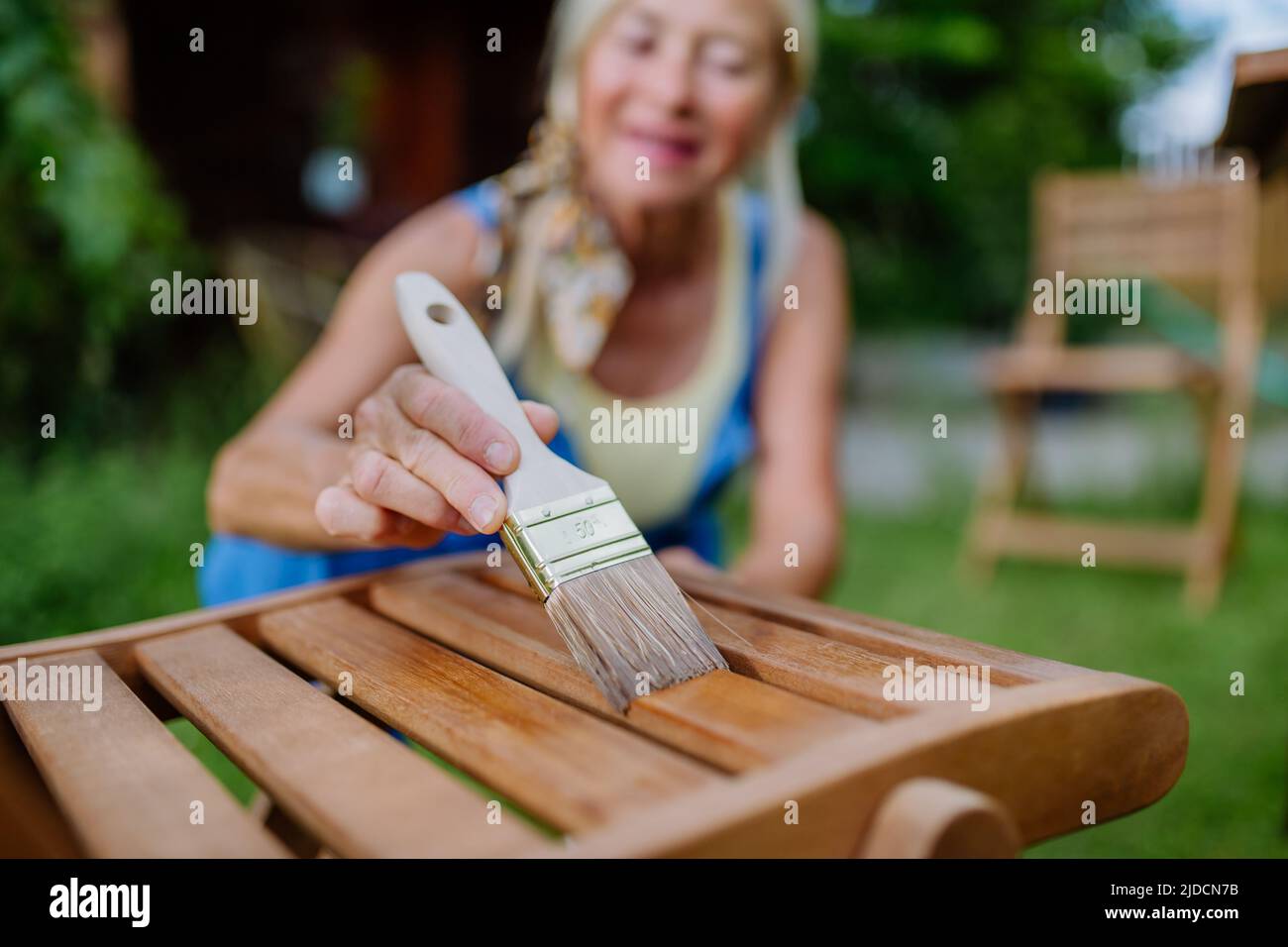 Senior woman cleaning and renovating garden furniture and getting the