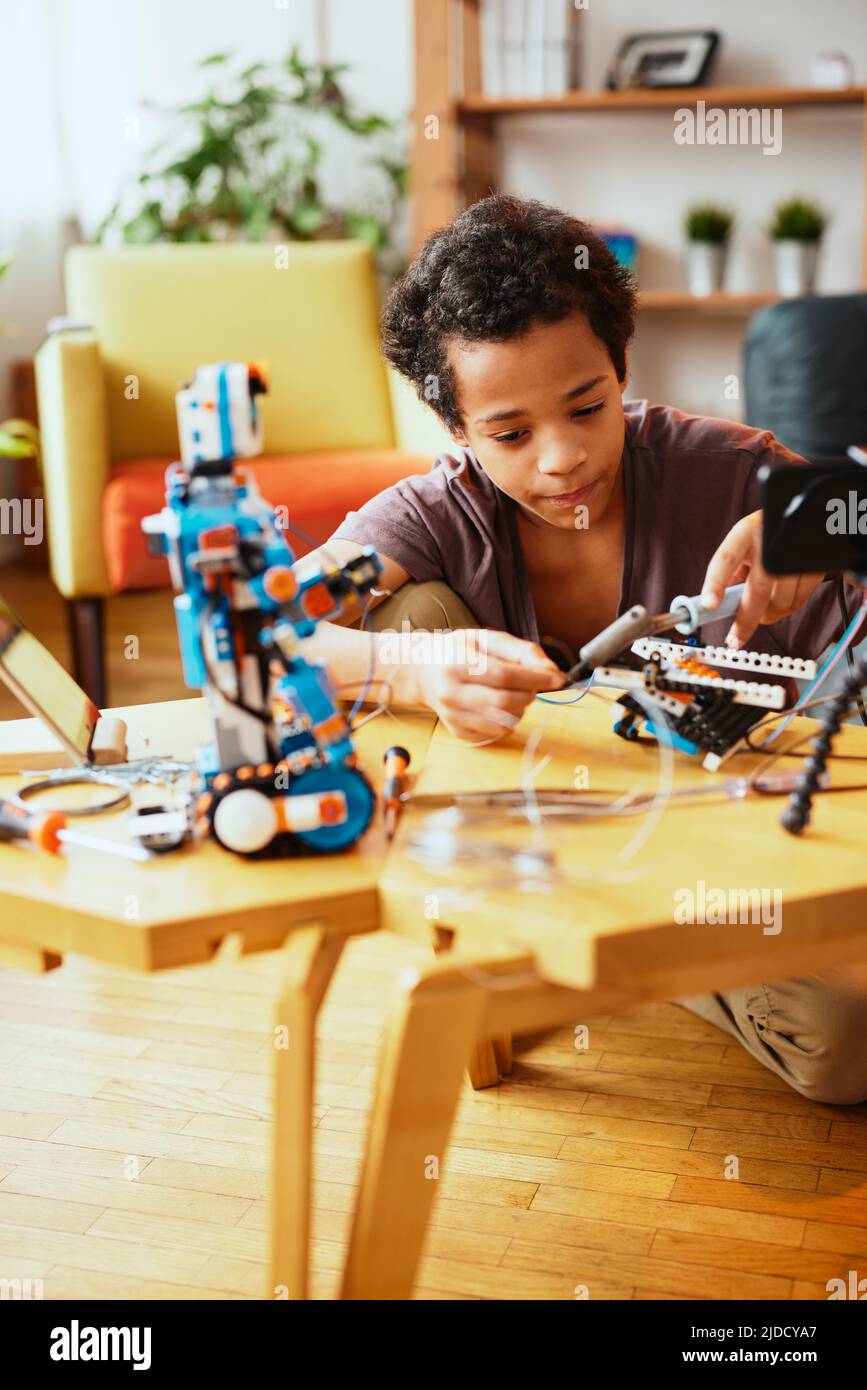 Dedicated African schoolboy making a robot at home for science class ...