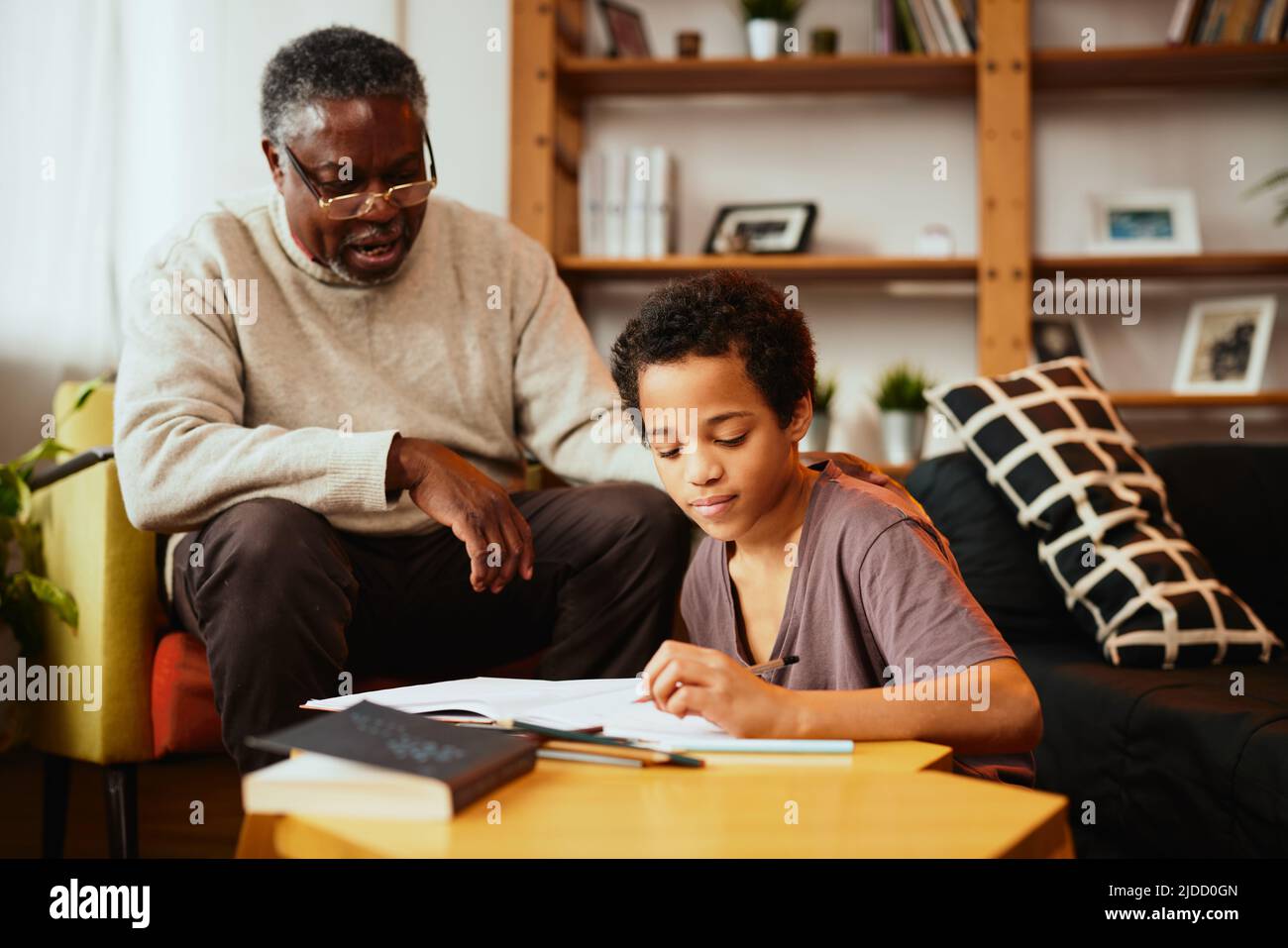 A grandfather looking at his grandchild's homework and checking on him at home. Stock Photo