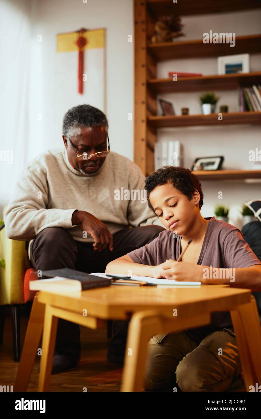 A grandfather looking at his grandchild's homework and checking on him at home. Stock Photo