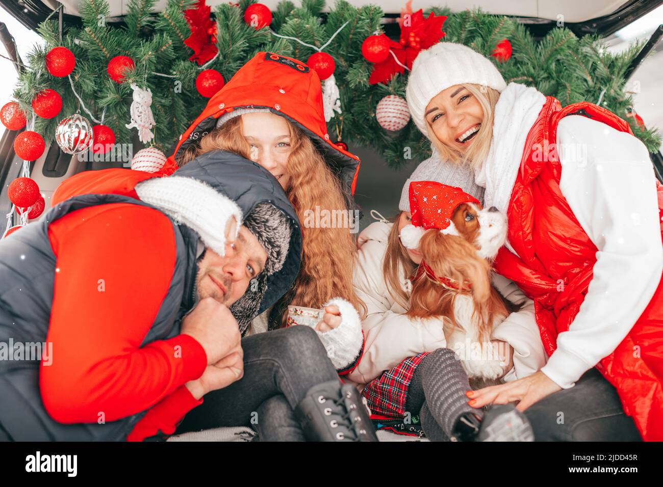 Happy family enjoying Christmas moments in car trunk with red decoration, children are happy with two parents and dog Cavalier King Charles Spaniel Stock Photo