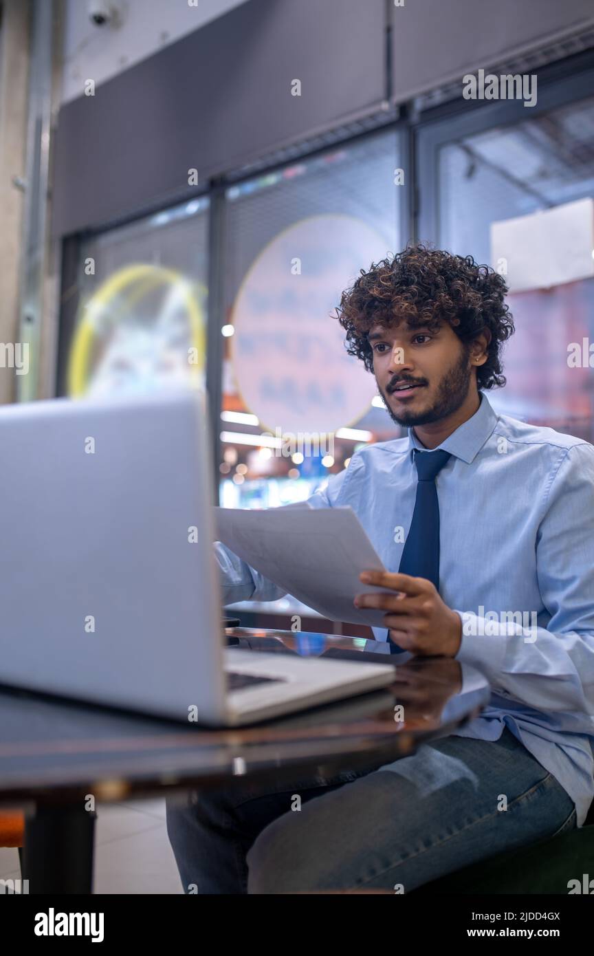 Man with papers looking at laptop sitting at table Stock Photo