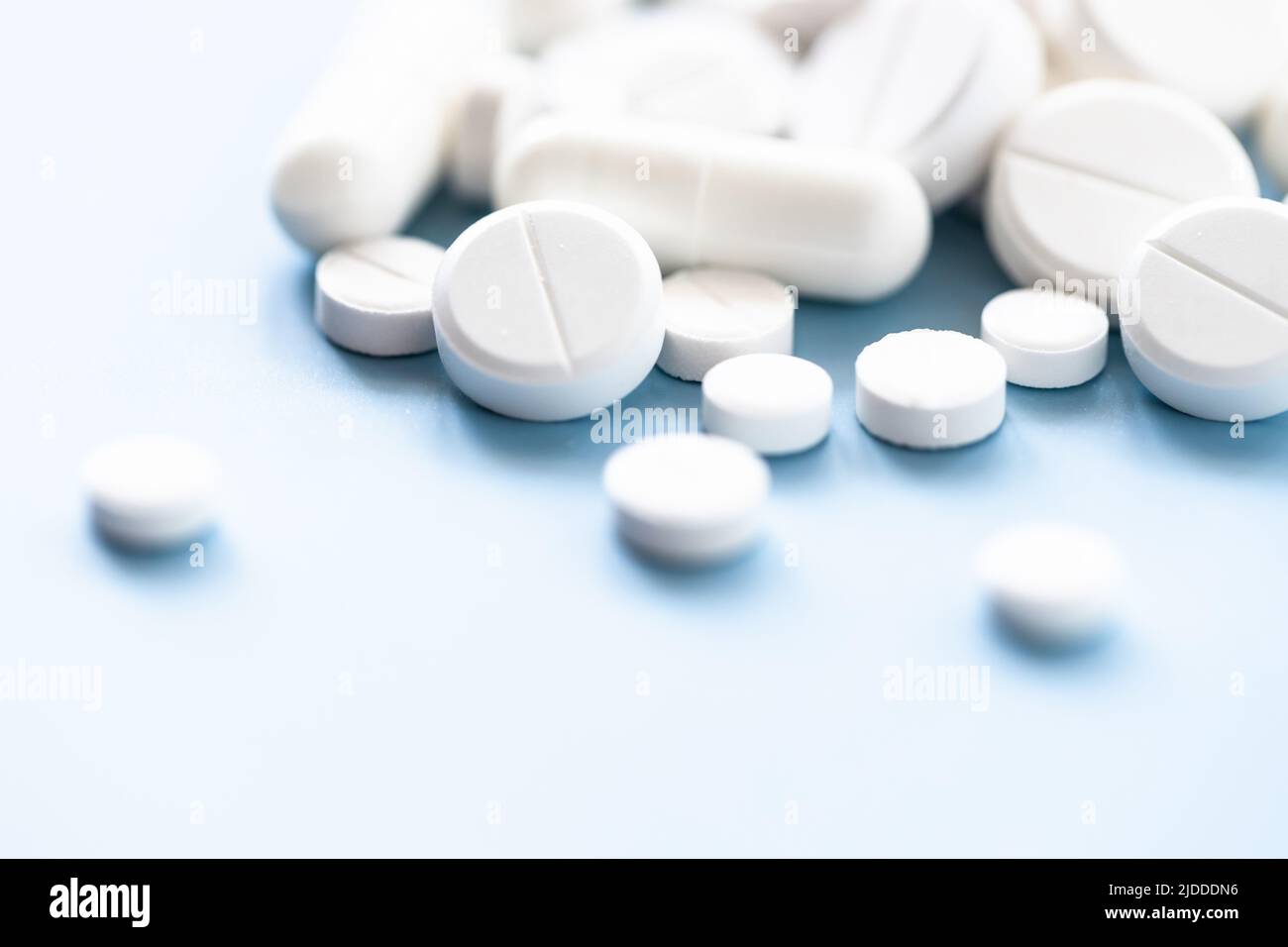 Various white pills on blue background against backlight. Stock Photo