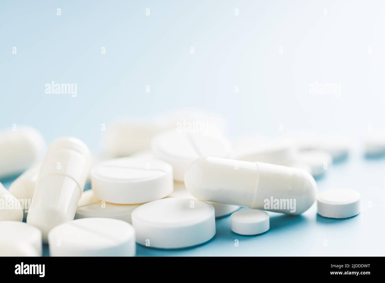 Different shapes white pills on blue background. Stock Photo