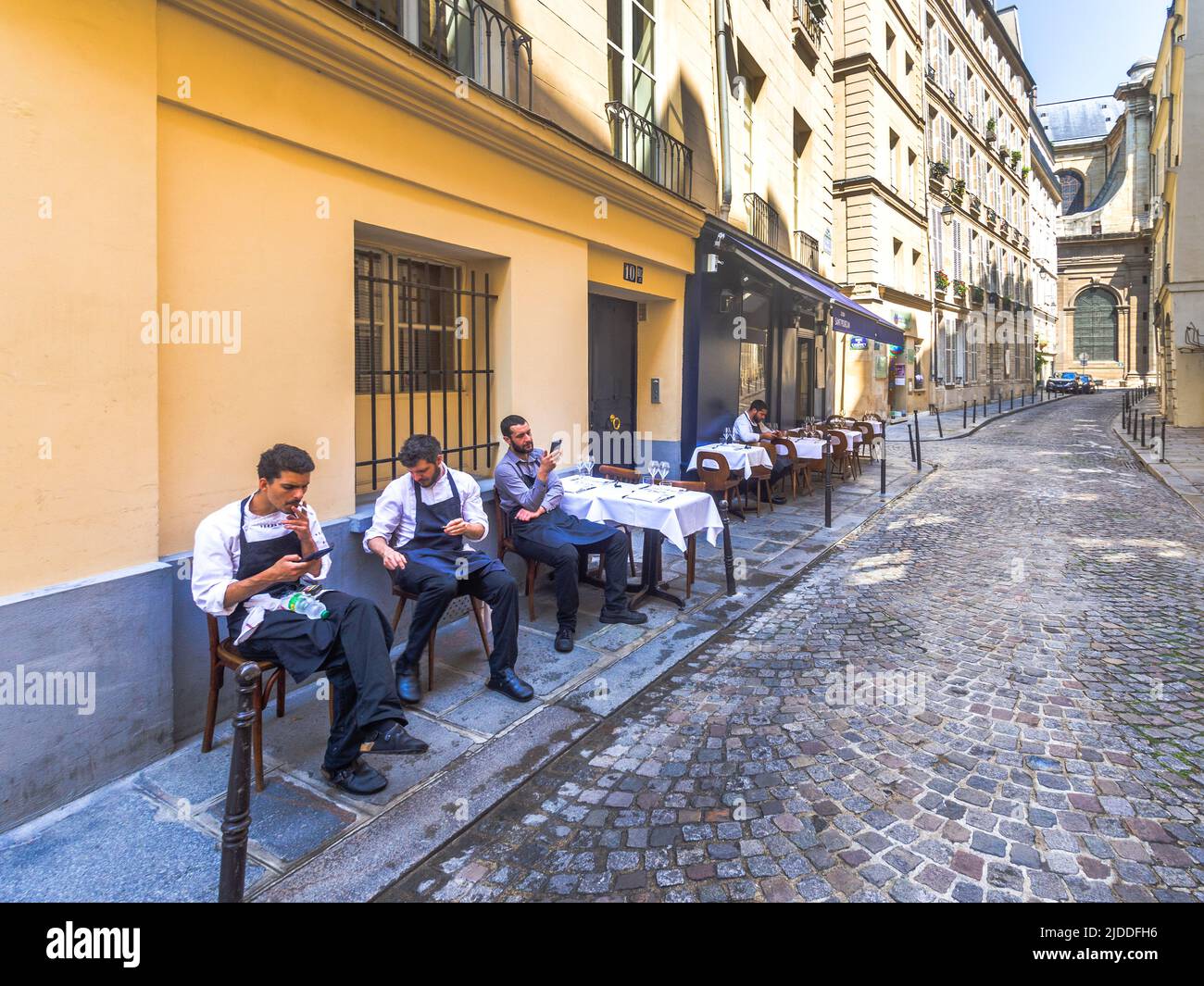 Waiters relaxing outside restaurant before clients arrive for lunch - Rue Servandoni, Paris 6, France. Stock Photo