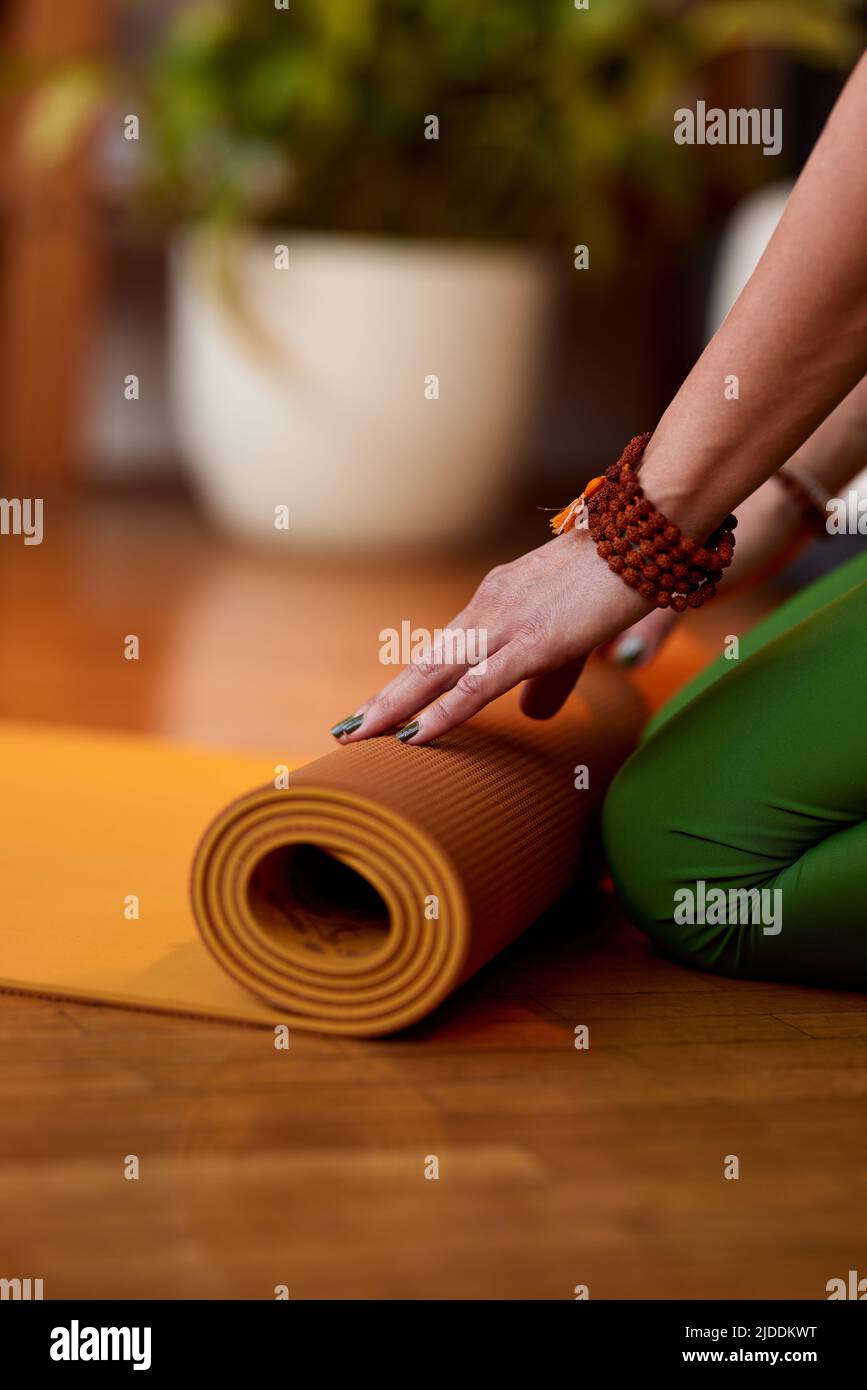 Close up of yogi woman's hands rolling up a yoga mat at home. Hands rolling yoga mat. Stock Photo