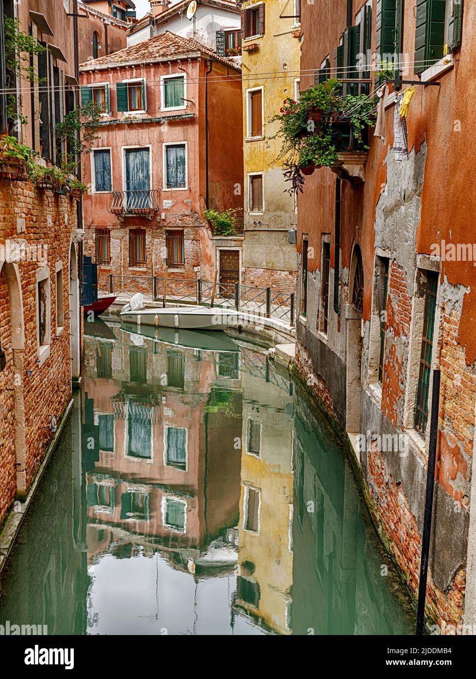Calm water in a narrow Venice canal reflects the buildings on both sides. Stock Photo