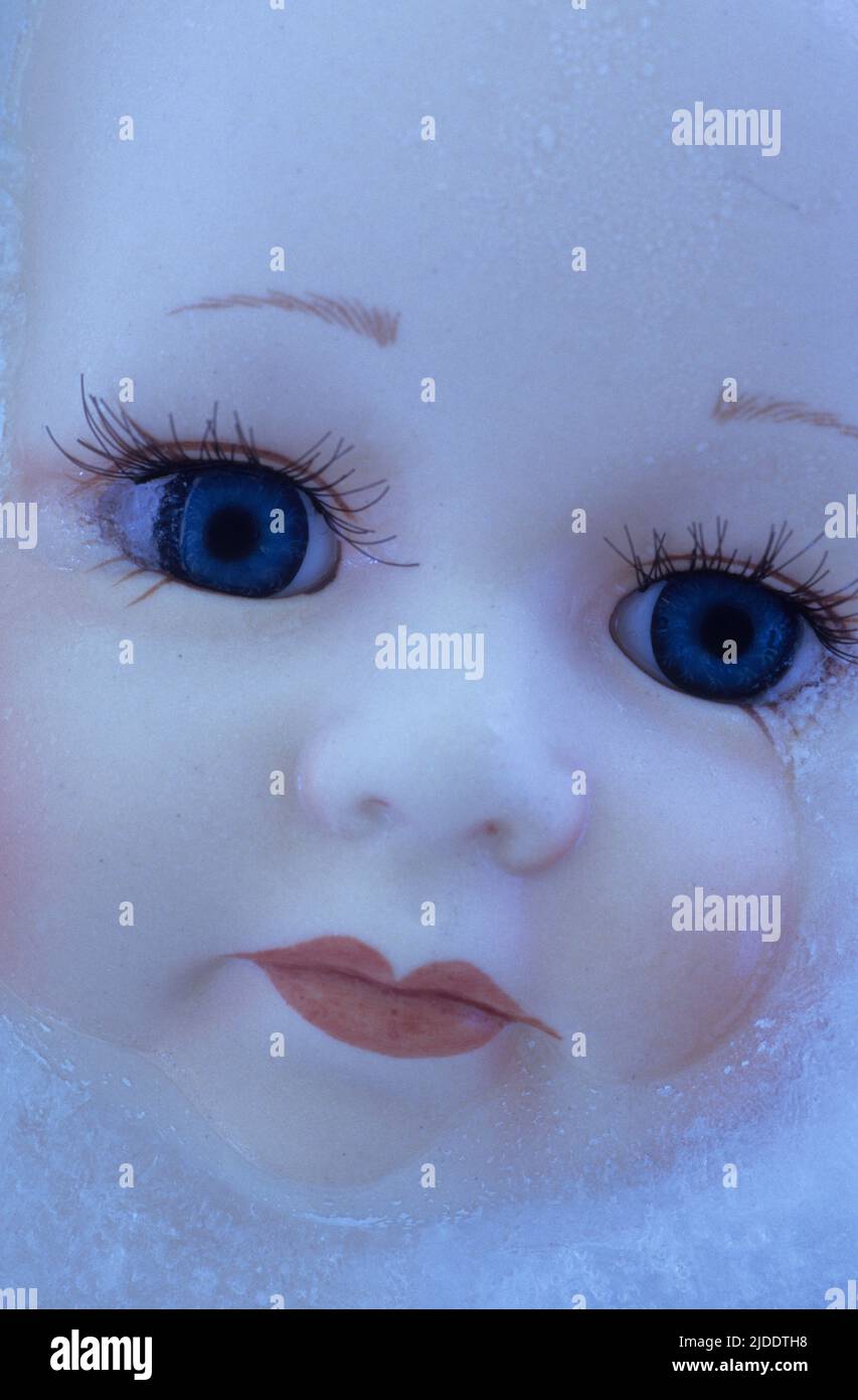 Face of modern toy doll with big blue eyes and long eyelashes lying in sheet of ice Stock Photo