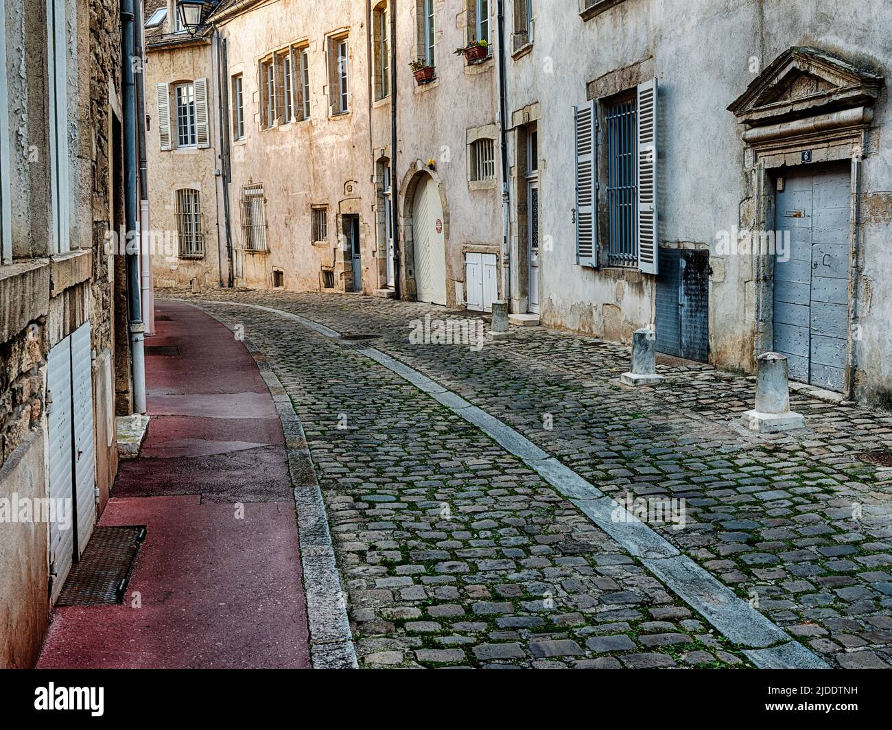 A red sidewalk runs alongside an old cobblestone street in Beaune, France. Stock Photo