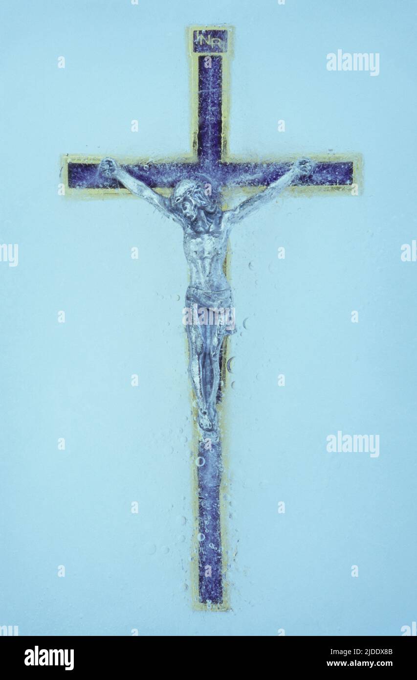 Blue enamel and gold crucifix with Jesus Christ suspended on it embedded in sheet of ice Stock Photo