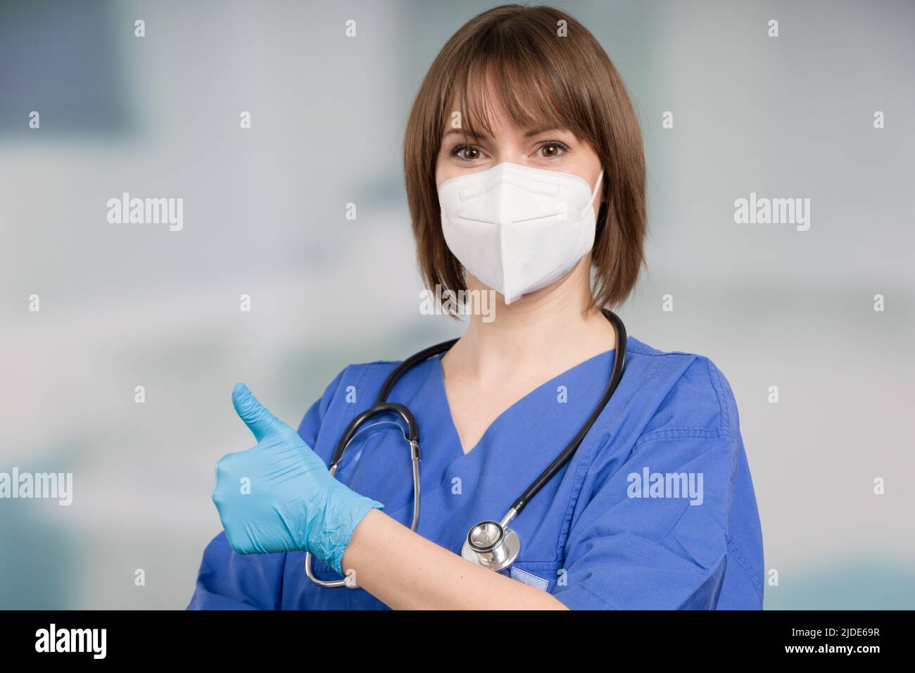 female doctor or icu nurse with medical face mask and medical gloves shows thumbs up Stock Photo