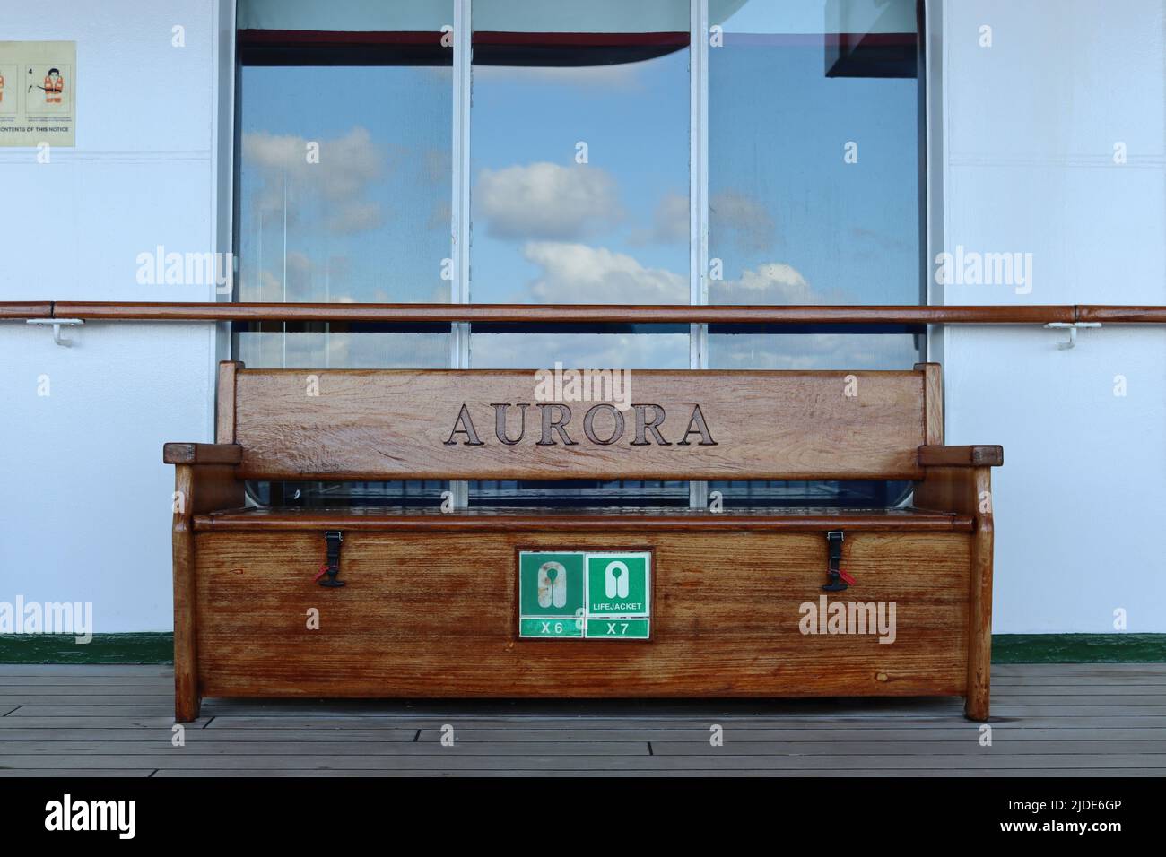 The P&O cruise ship Aurora’s promenade deck with a wooden bench seat with the ship’s name carved name on it. Stock Photo