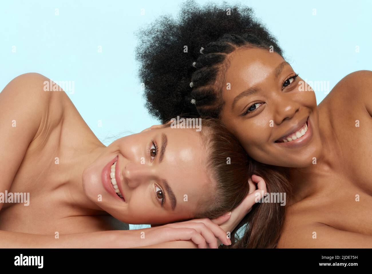 Young beautiful caucasian and african women posing lying on top of each other, face to face. Lifestyle of different nationalities, people concept Stock Photo